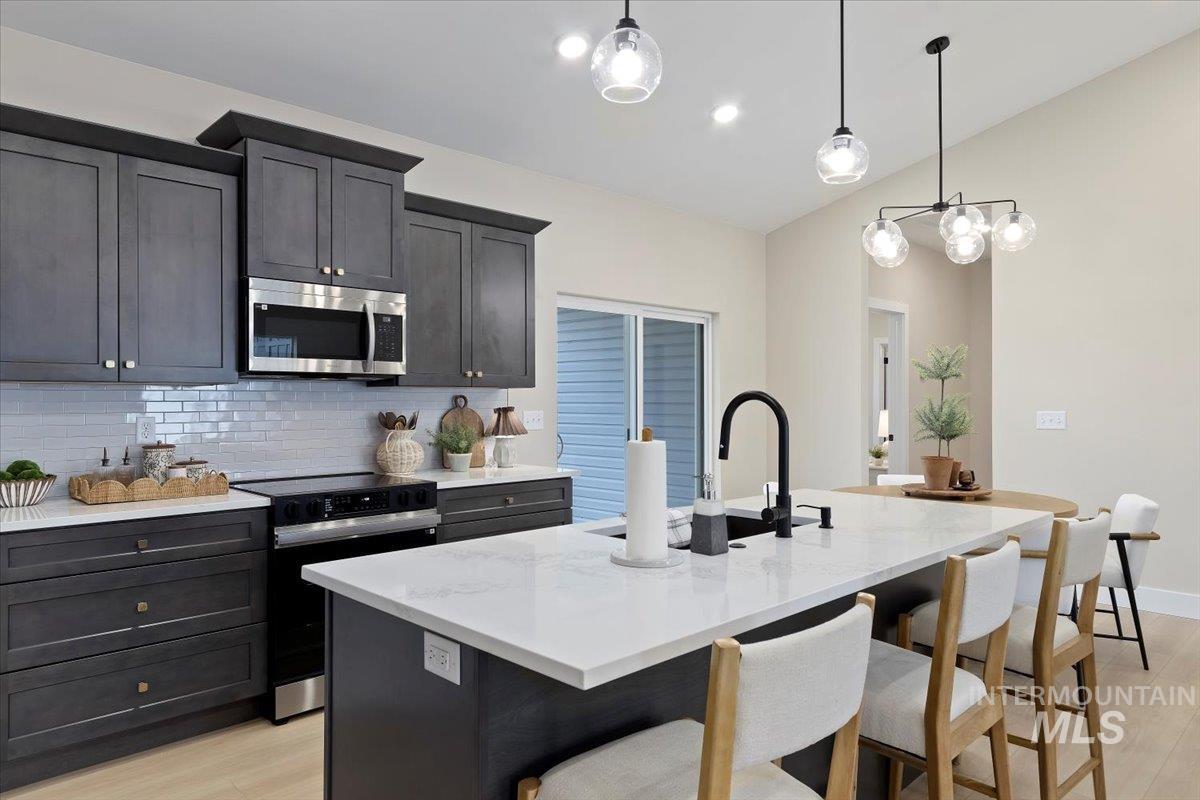 Kitchen featuring range with electric stovetop, light stone countertops, stainless steel microwave, a kitchen island with sink, and lofted ceiling