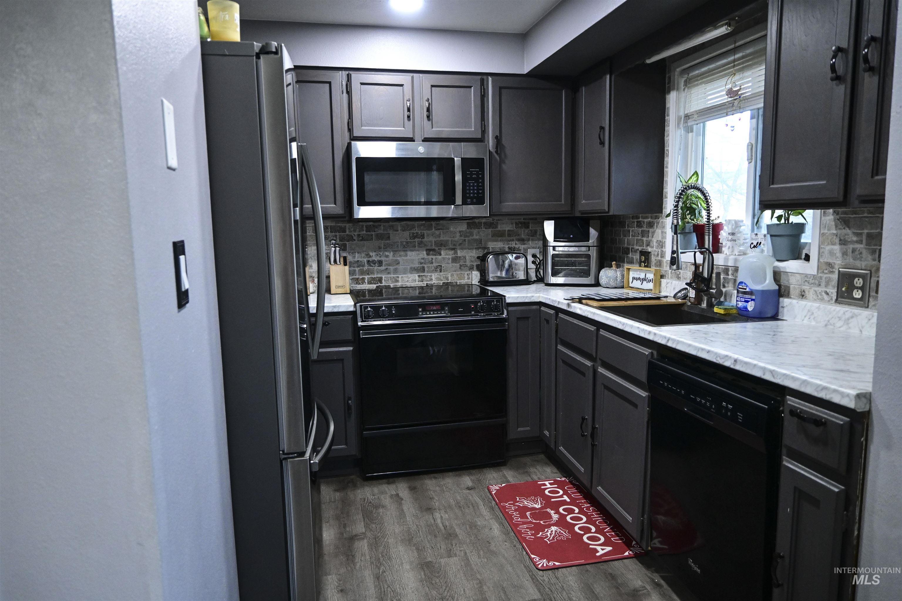 Kitchen featuring black appliances, decorative backsplash, dark wood-style flooring, gray cabinets, and a textured wall