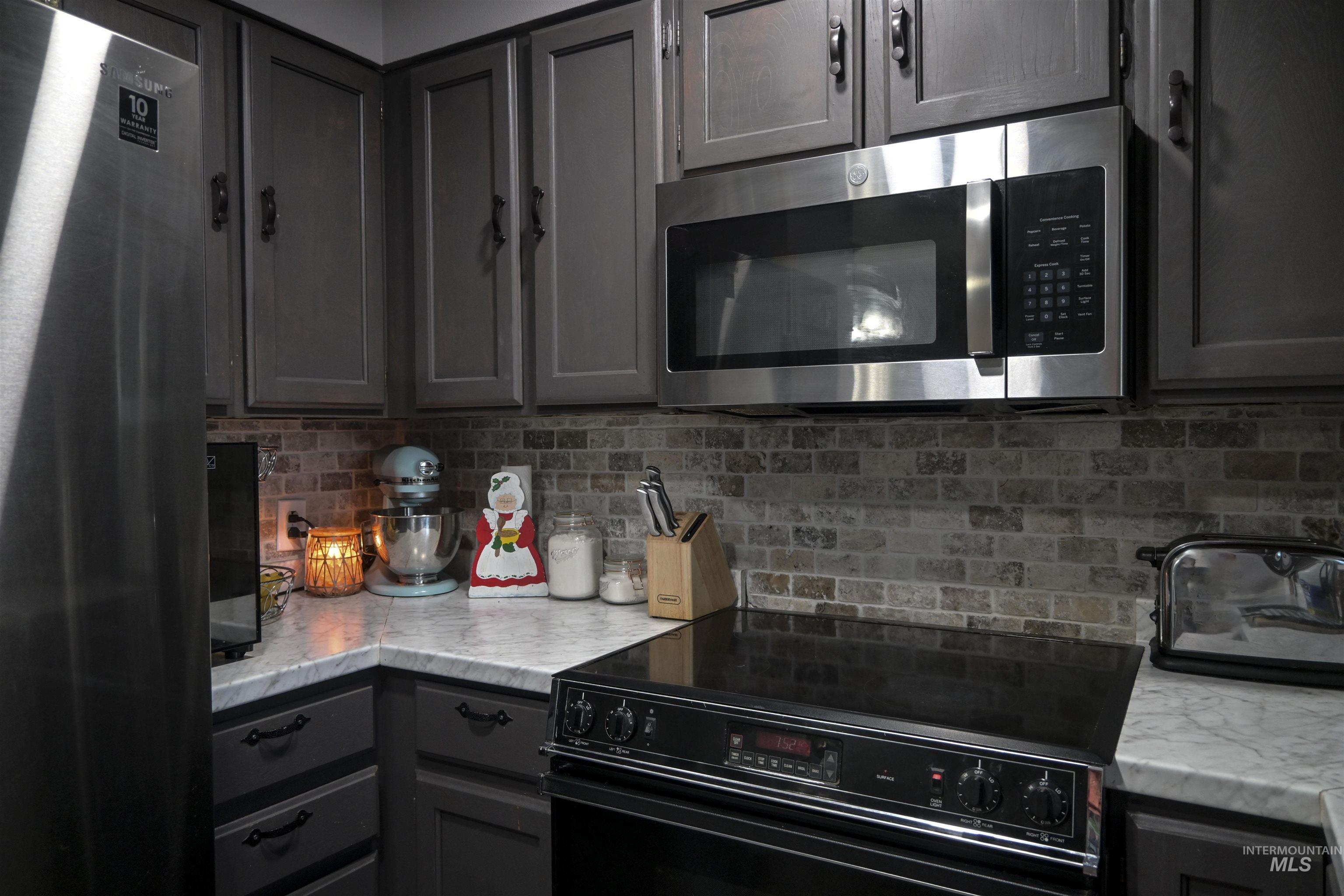 Kitchen featuring gray cabinetry, stainless steel appliances, light stone counters, and decorative backsplash