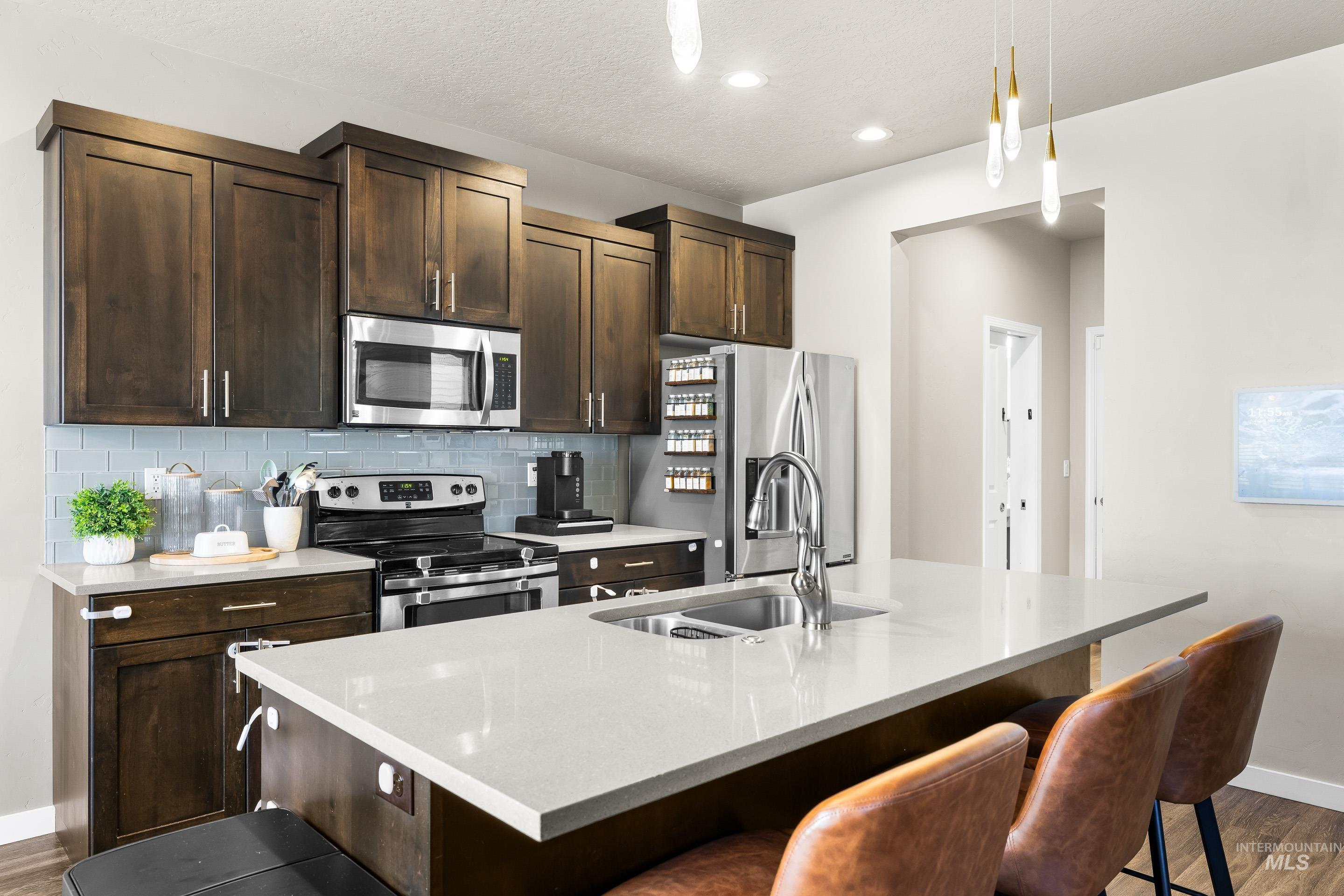 Kitchen featuring dark brown cabinets, dark wood-type flooring, a kitchen island with sink, appliances with stainless steel finishes, and a textured ceiling
