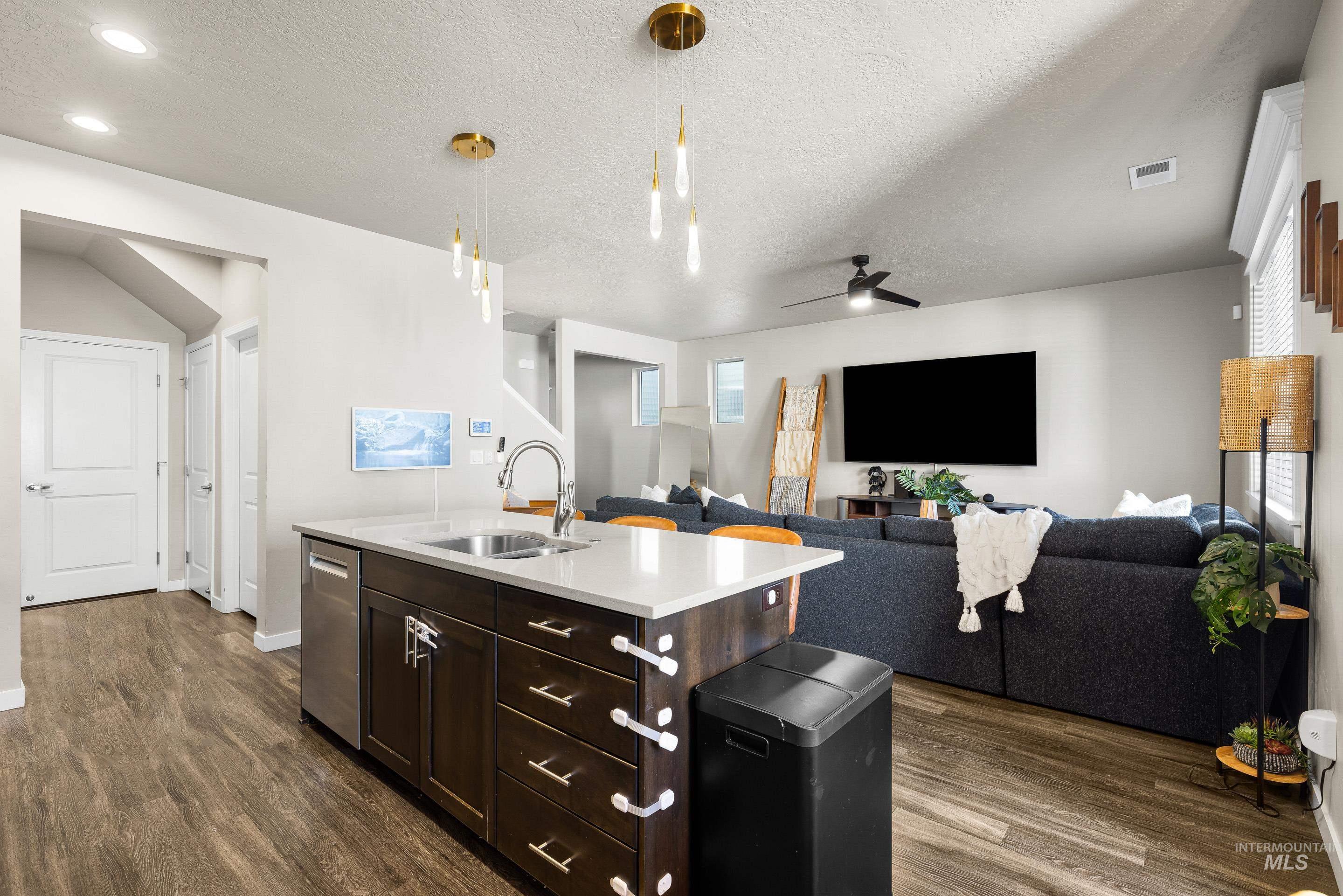 Kitchen featuring dark brown cabinets, a textured ceiling, ceiling fan, decorative light fixtures, and an island with sink