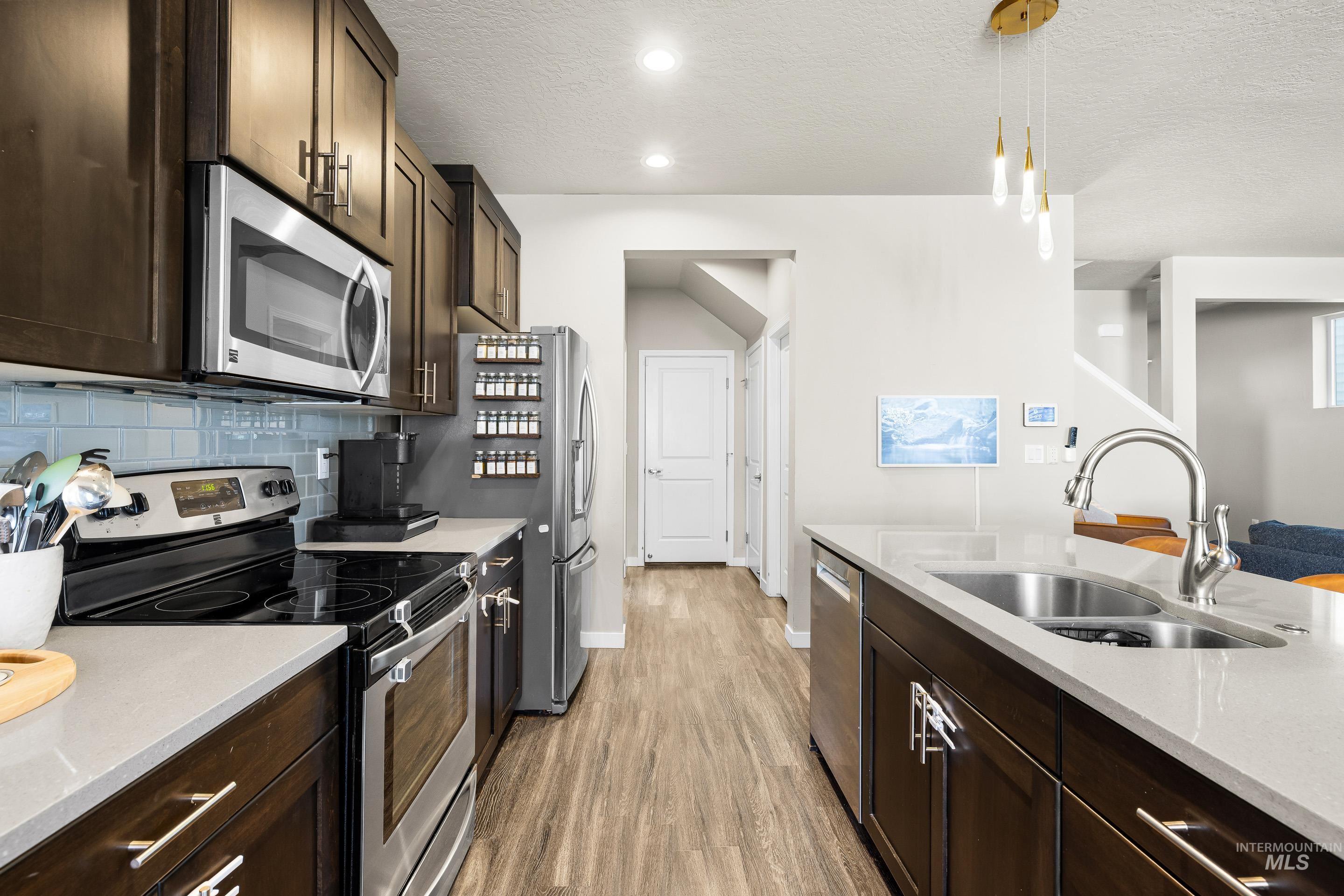 Kitchen featuring dark brown cabinets, stainless steel appliances, light stone countertops, pendant lighting, and a textured ceiling