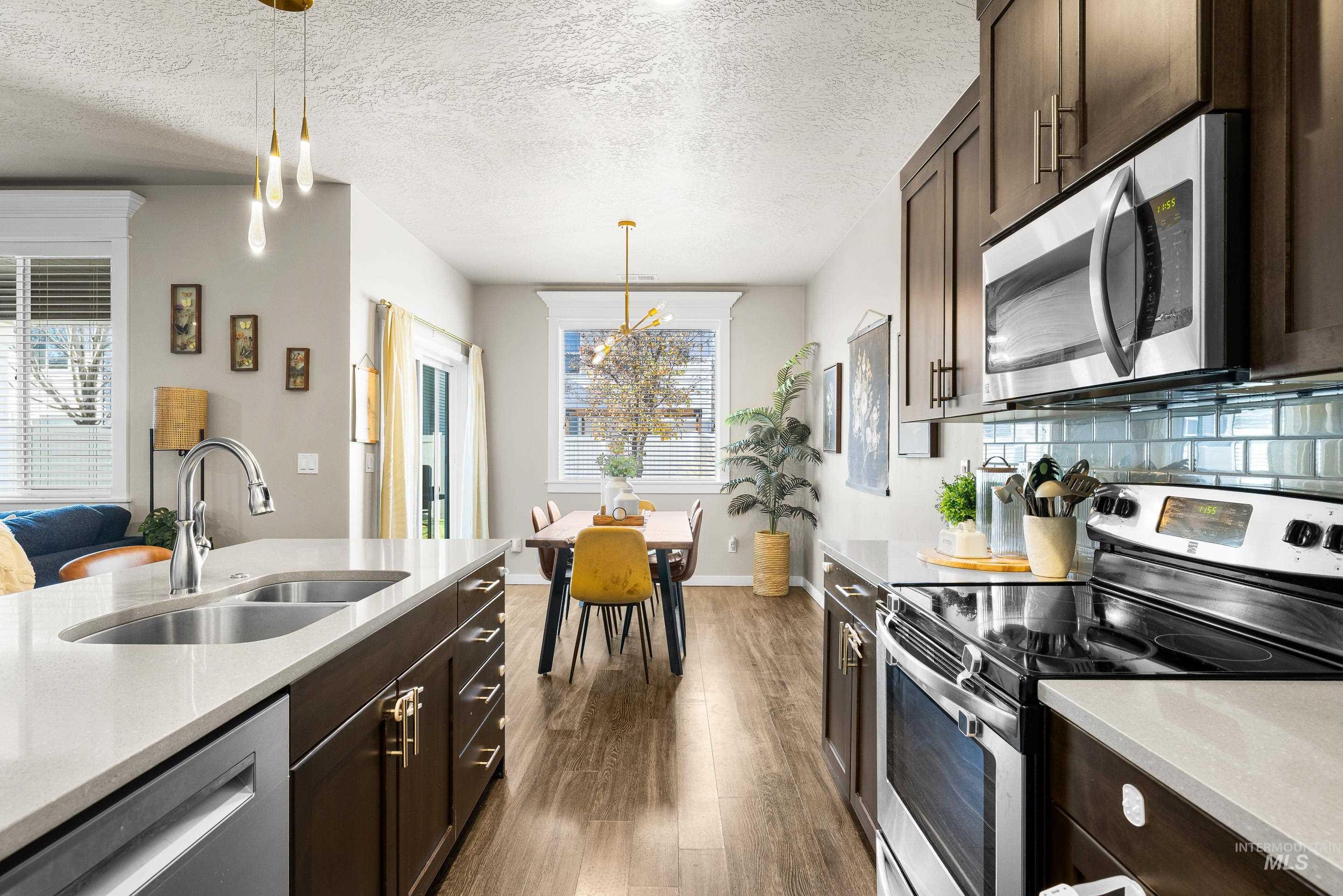 Kitchen with dark brown cabinets, stainless steel appliances, light stone countertops, a textured ceiling, and dark wood-type flooring