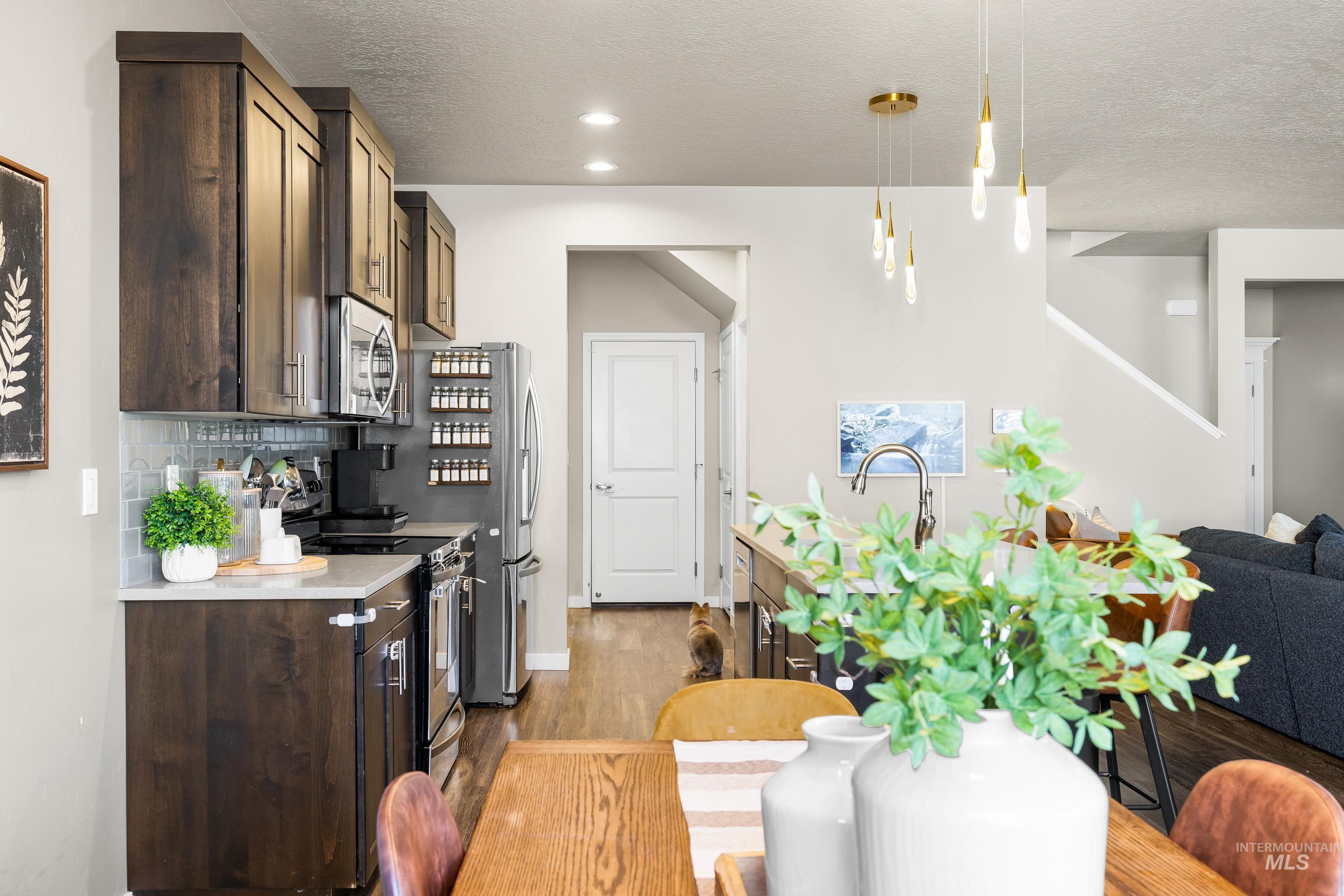 Kitchen with dark brown cabinets, light countertops, tasteful backsplash, appliances with stainless steel finishes, and decorative light fixtures