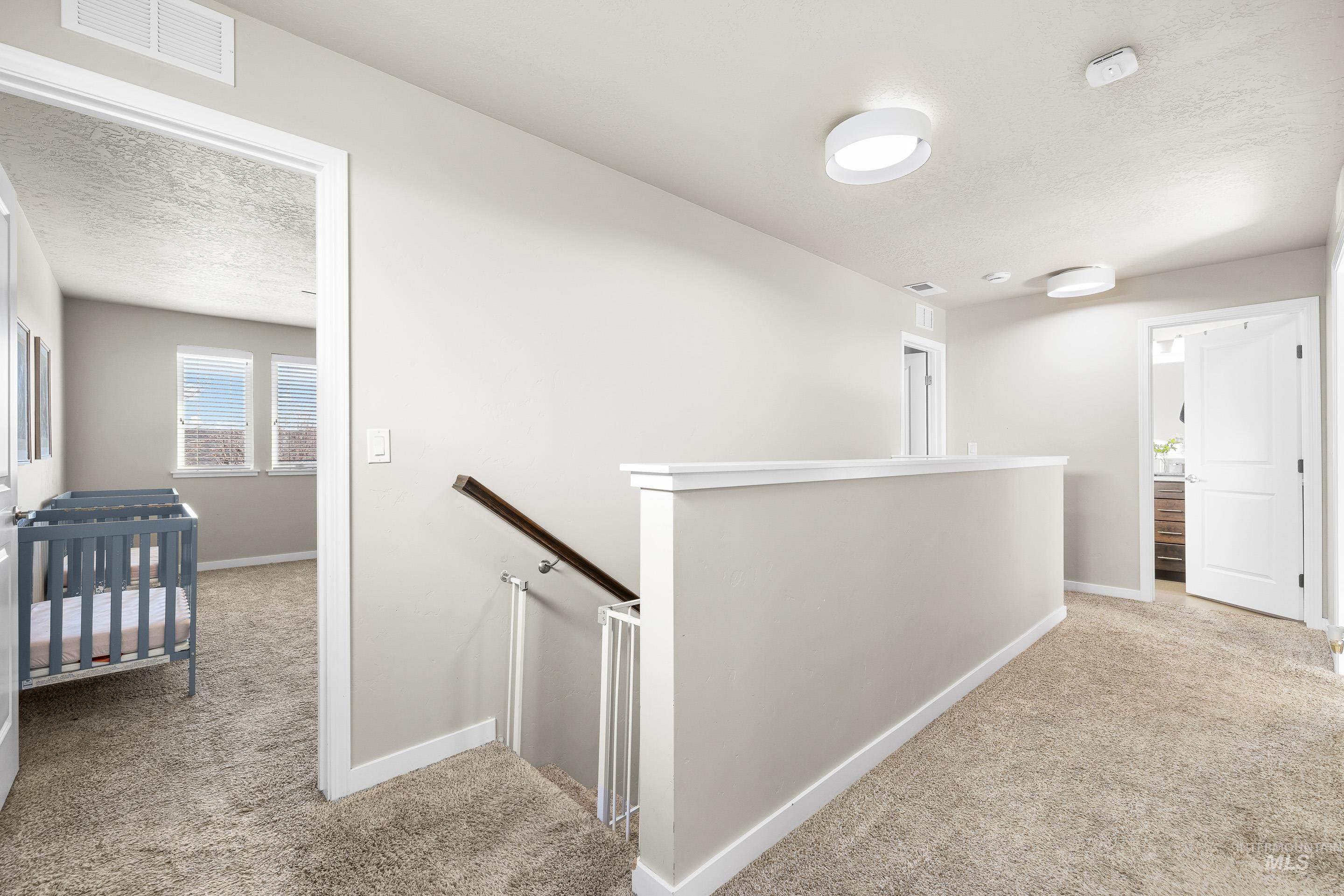 Hallway with an upstairs landing, light carpet, and a textured ceiling