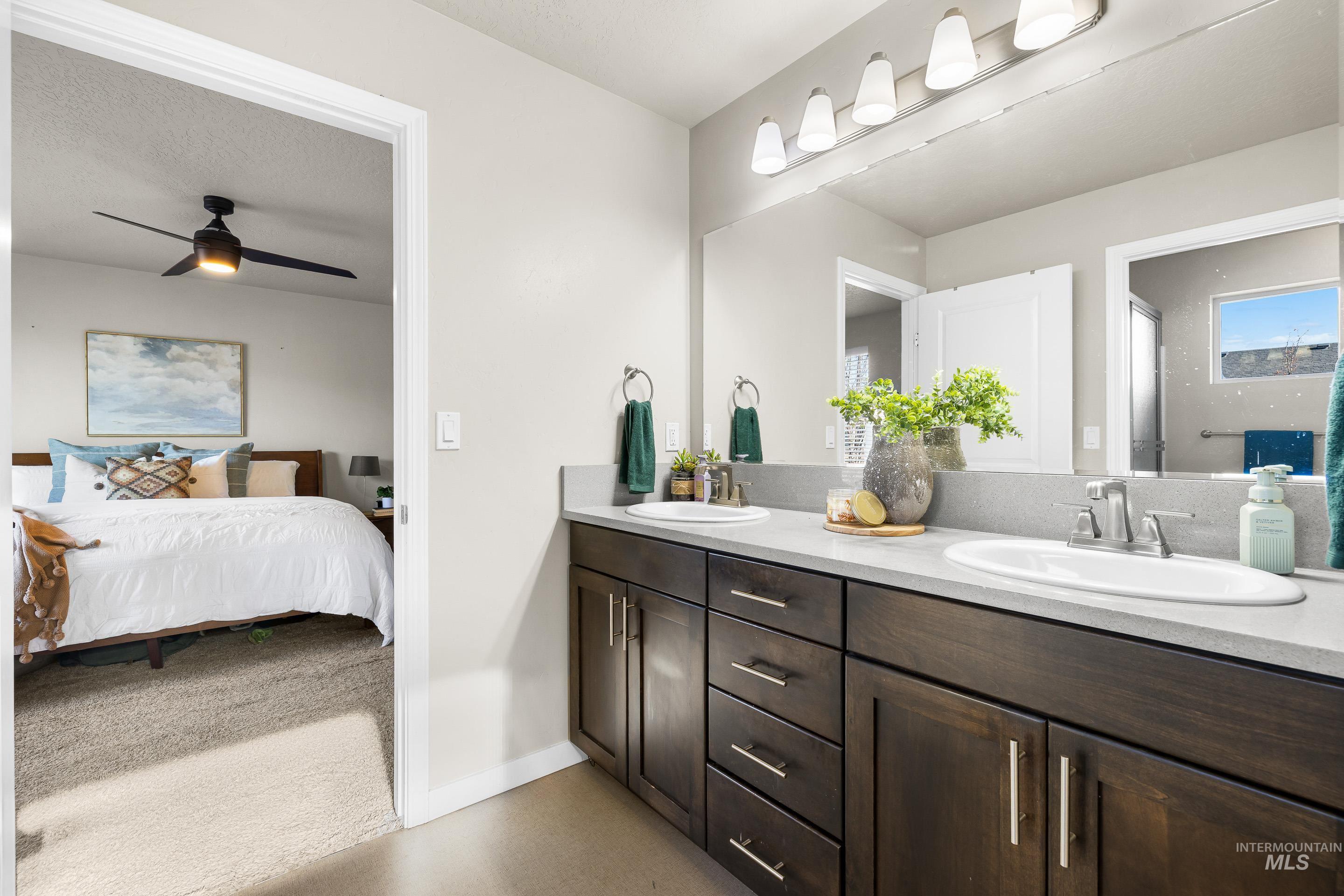Ensuite bathroom with double vanity, ceiling fan, light carpet, and a textured ceiling