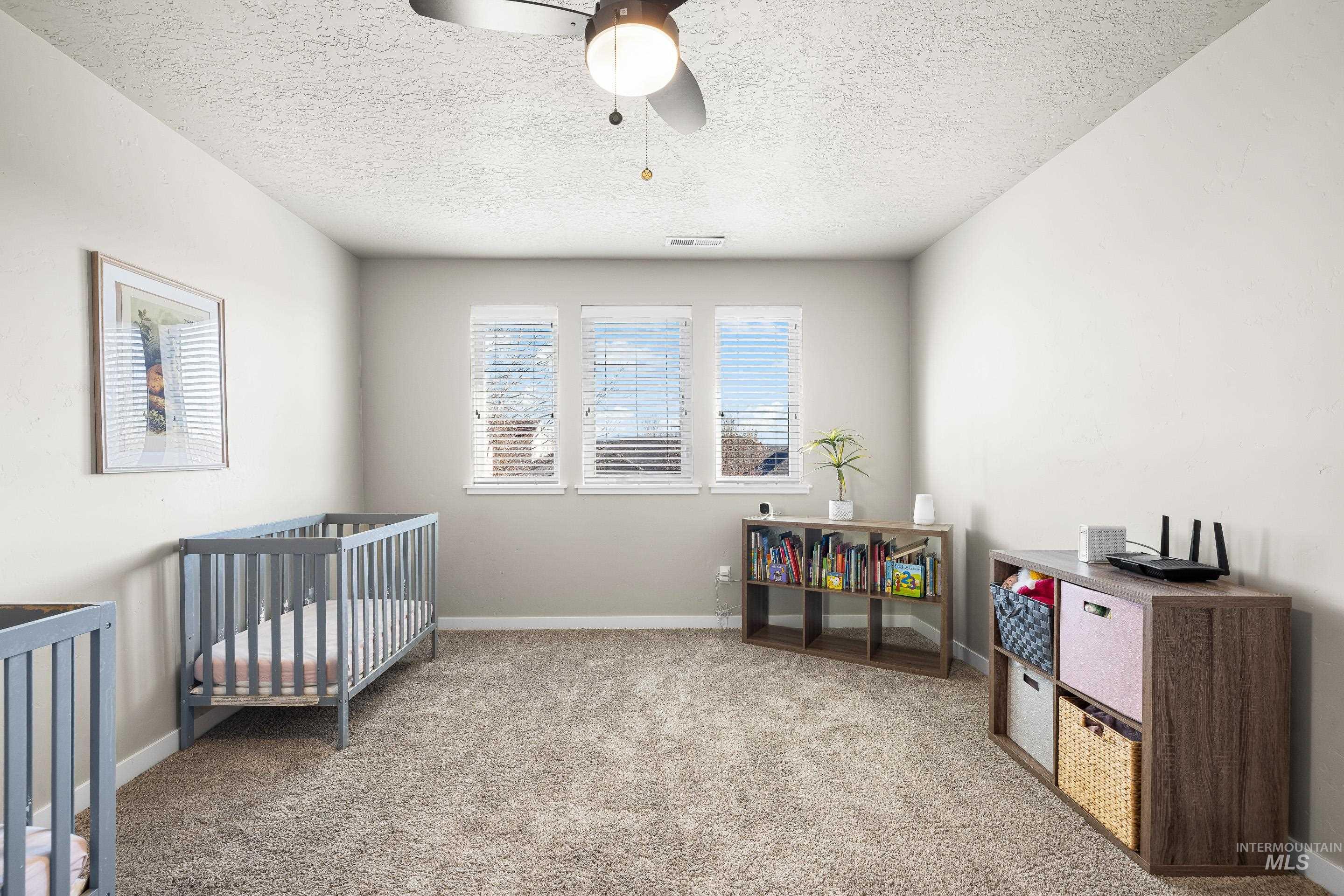 Bedroom featuring carpet floors, a ceiling fan, a textured ceiling, and a crib