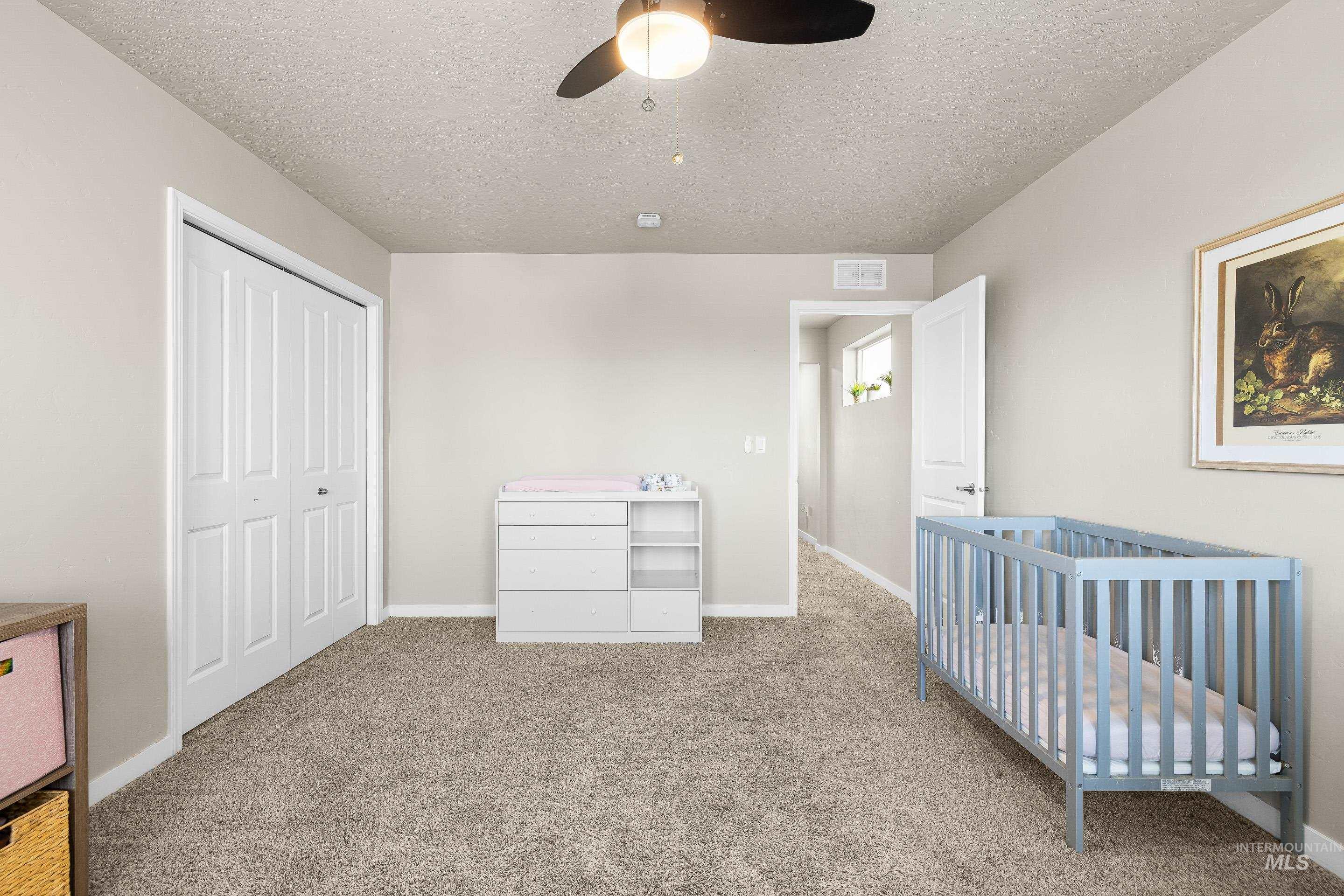 Unfurnished bedroom featuring carpet flooring, a closet, a ceiling fan, a nursery area, and a textured ceiling