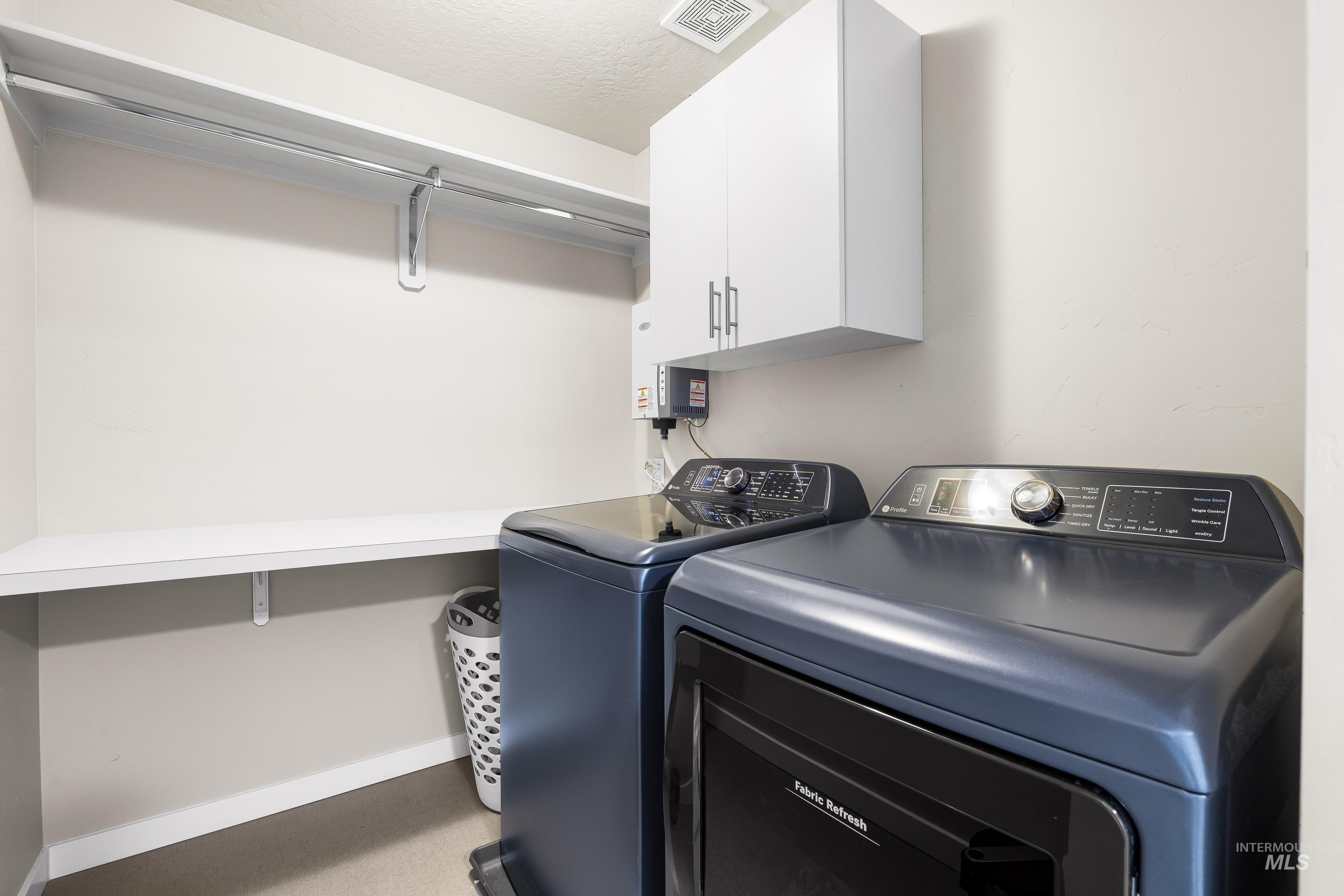 Washroom featuring washing machine and clothes dryer, cabinet space, and tankless water heater