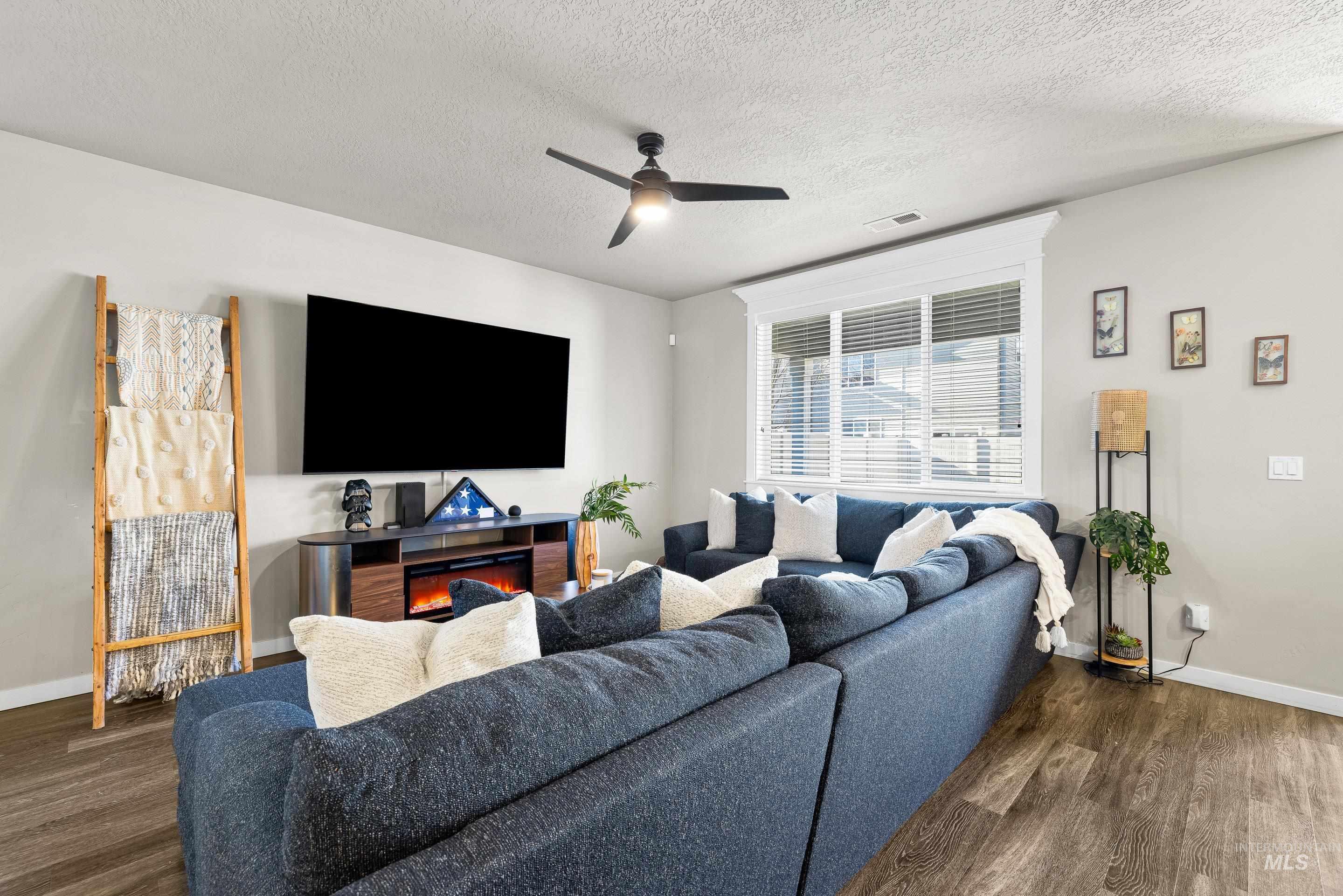 Living room featuring dark wood finished floors, a textured ceiling, and ceiling fan