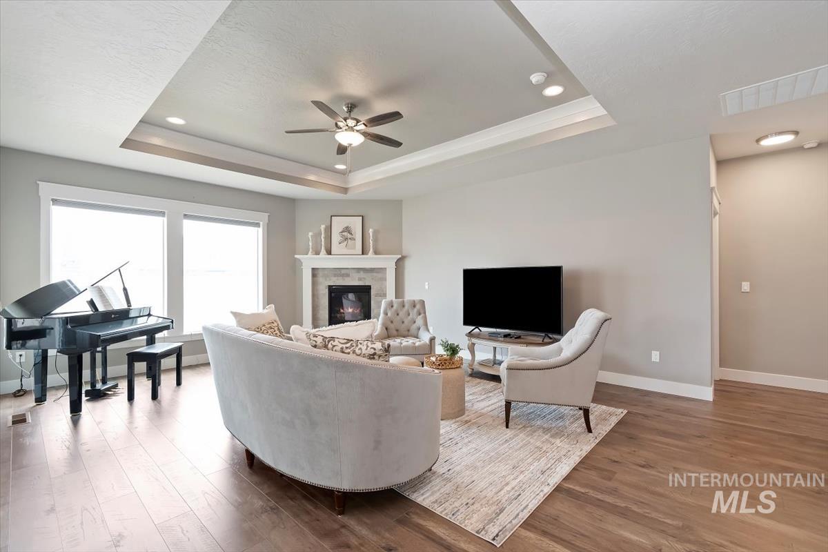 Living room with ceiling fan, a tray ceiling, light wood-style flooring, a fireplace, and recessed lighting