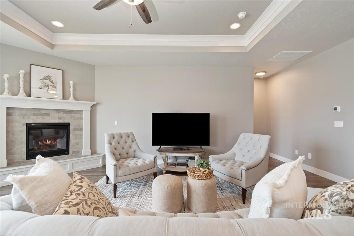 Living area featuring ornamental molding, a raised ceiling, a glass covered fireplace, ceiling fan, and wood finished floors