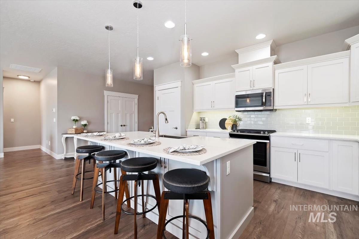 Kitchen featuring appliances with stainless steel finishes, a kitchen island with sink, hanging light fixtures, a kitchen bar, and white cabinets