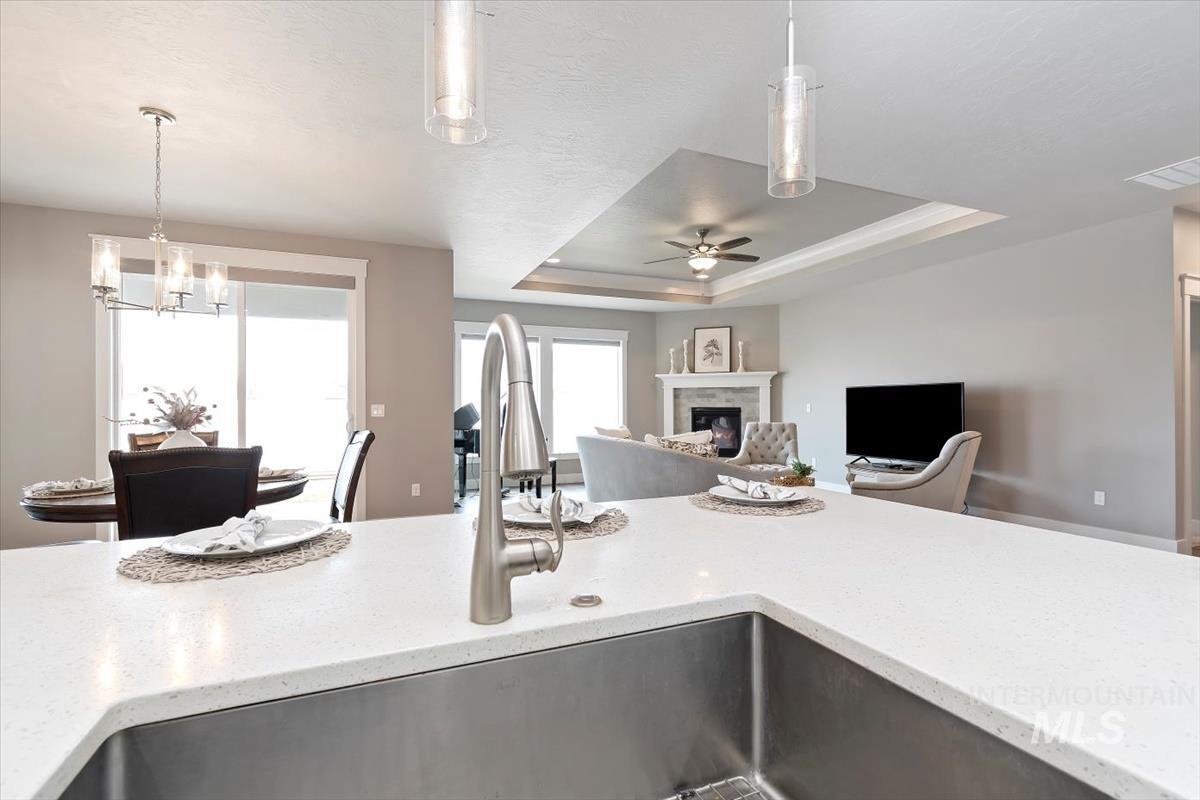 Kitchen with a raised ceiling, hanging light fixtures, open floor plan, a glass covered fireplace, and light stone counters