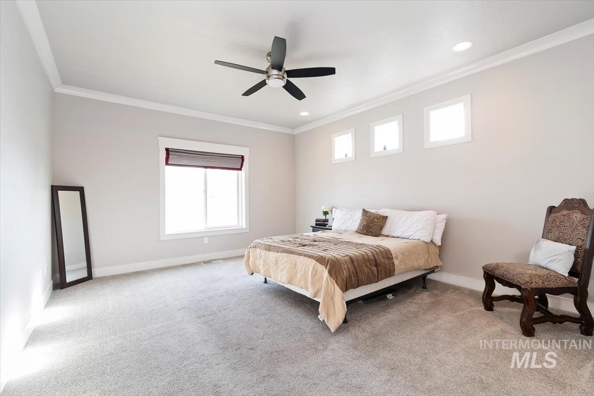 Bedroom with ornamental molding, light colored carpet, and ceiling fan
