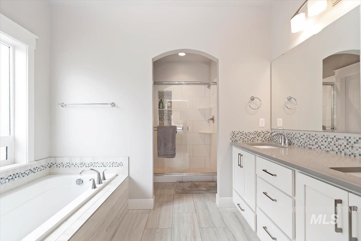 Full bathroom with double vanity, a garden tub, a shower stall, and backsplash