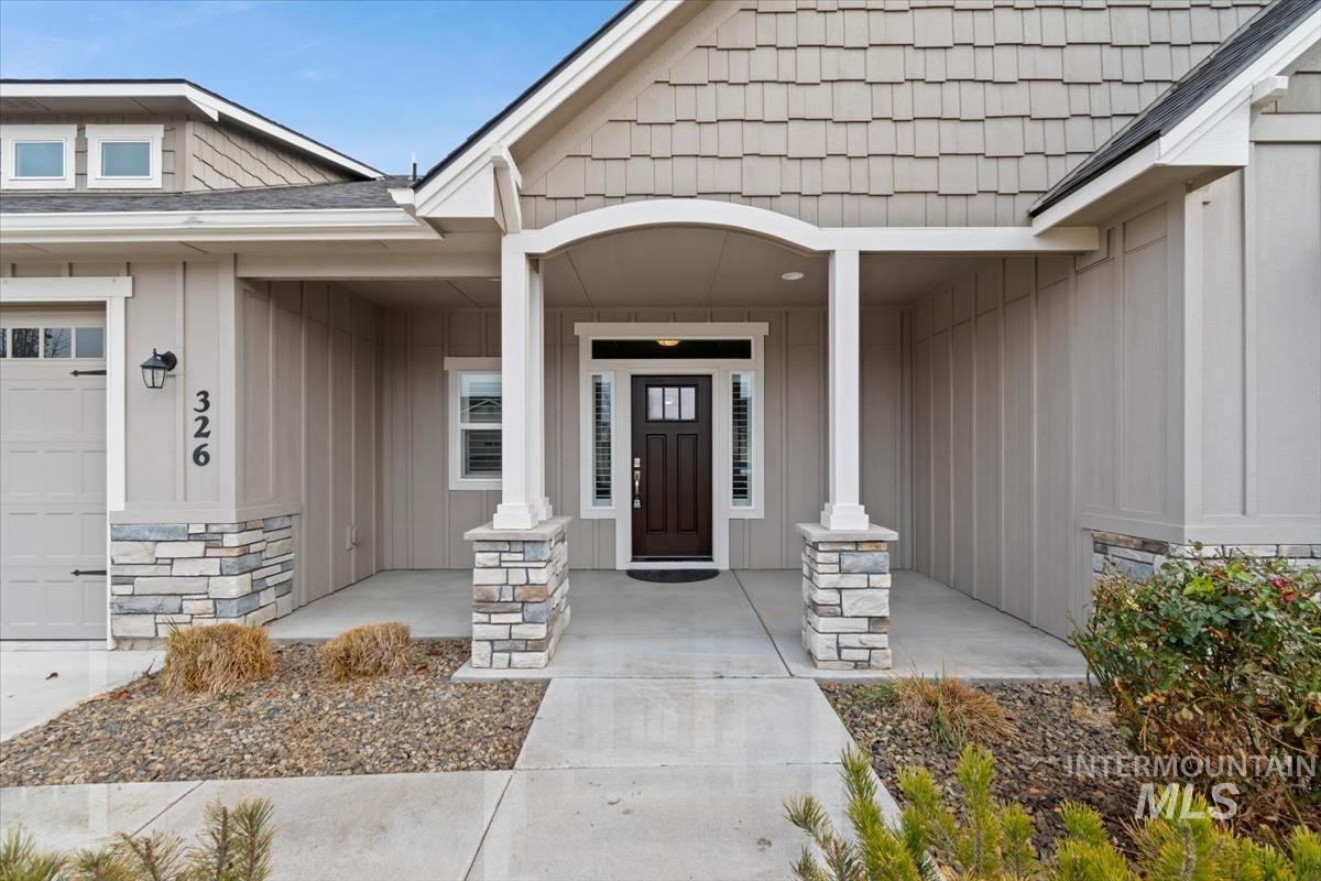 Doorway to property featuring board and batten siding, covered porch, a garage, and stone siding