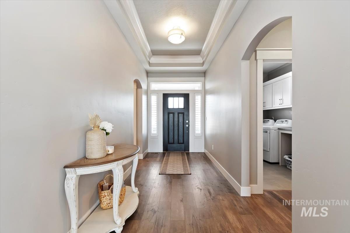 Foyer entrance with arched walkways, a raised ceiling, dark wood finished floors, and washer and clothes dryer