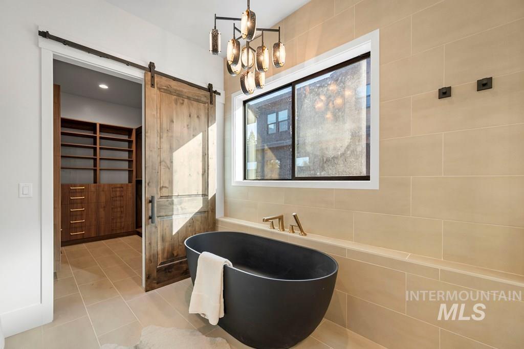 Bathroom with a chandelier, a soaking tub, tile patterned floors, tile walls, and a stall shower