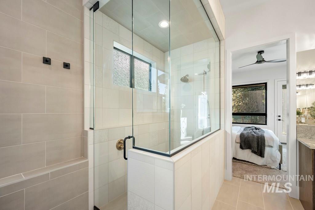 Ensuite bathroom featuring a stall shower, ceiling fan, vanity, and tile patterned floors