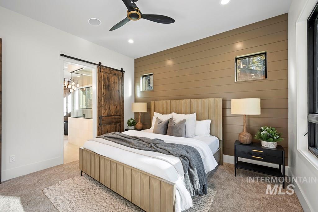 Bedroom featuring carpet floors, wooden walls, ceiling fan, a barn door, and an accent wall