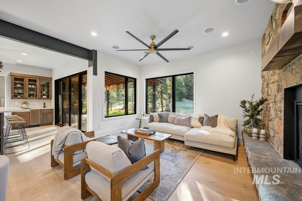 Living area featuring a stone fireplace, bar with sink, light wood finished floors, recessed lighting, and a ceiling fan