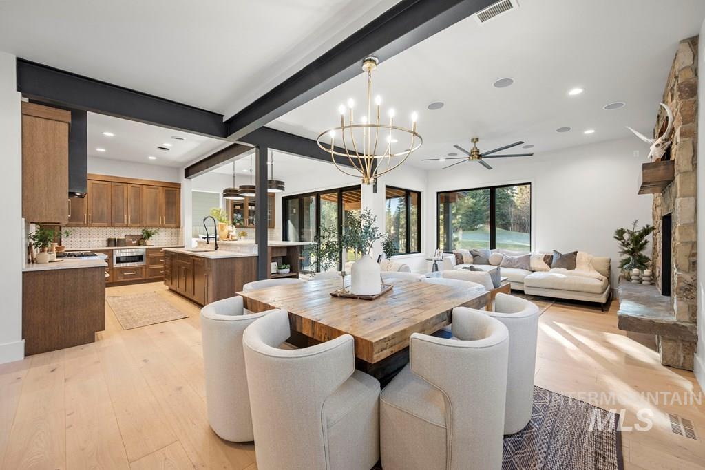 Dining room with a chandelier, recessed lighting, a stone fireplace, beamed ceiling, and light wood-style flooring