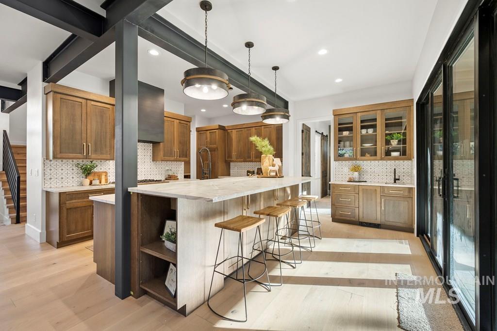 Kitchen with a kitchen bar, brown cabinetry, decorative light fixtures, a large island with sink, and light wood finished floors