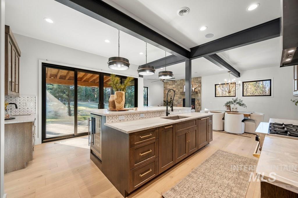 Kitchen with pendant lighting, dark brown cabinets, light stone counters, light wood-style flooring, and beam ceiling