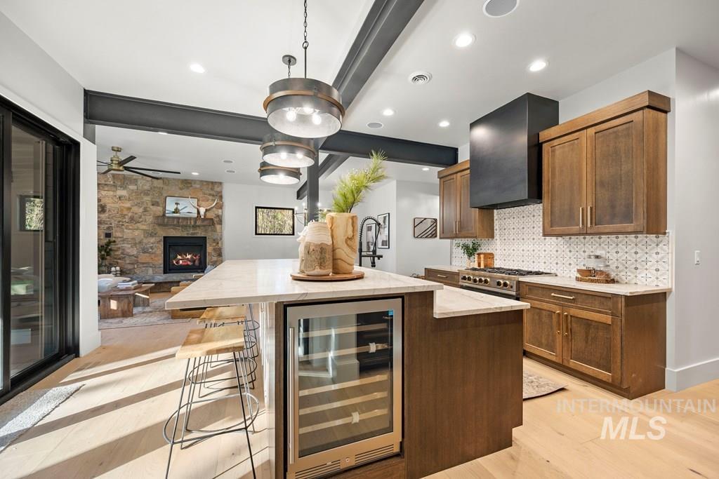 Kitchen featuring a kitchen island with sink, a breakfast bar area, beverage cooler, light stone counters, and beam ceiling