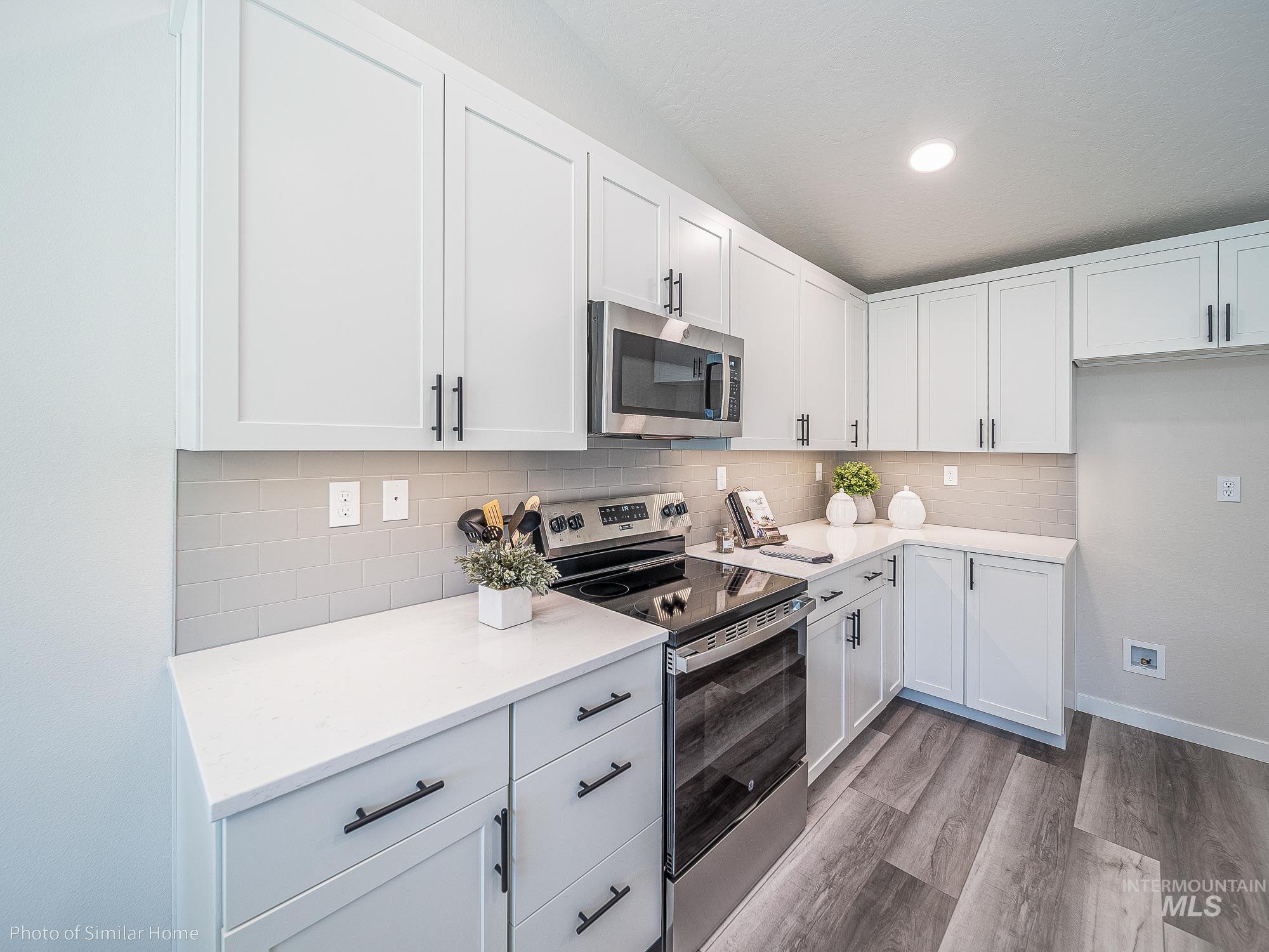 Kitchen with stainless steel appliances, decorative backsplash, white cabinetry, light countertops, and vaulted ceiling