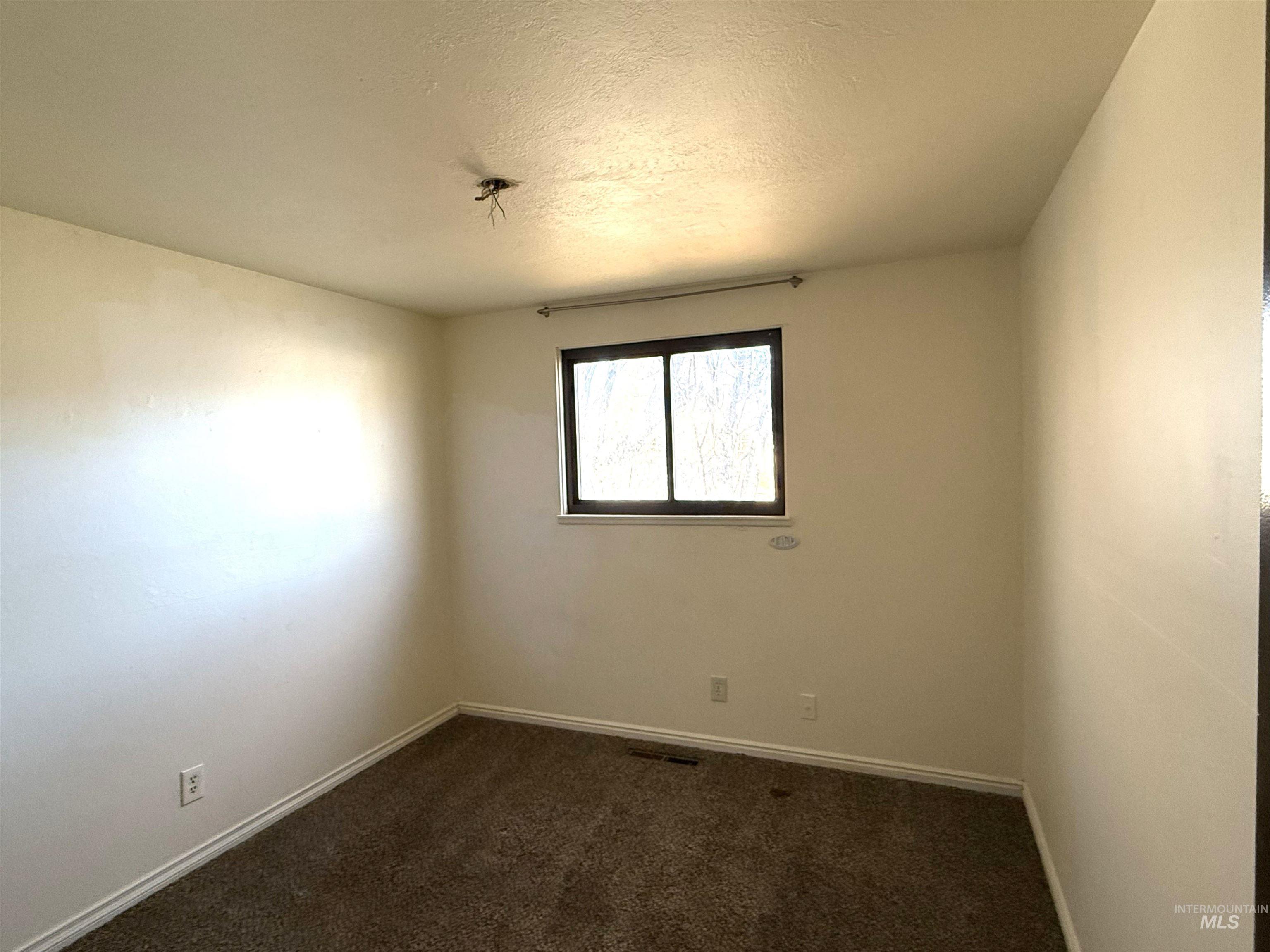 Empty room with dark colored carpet and a textured ceiling