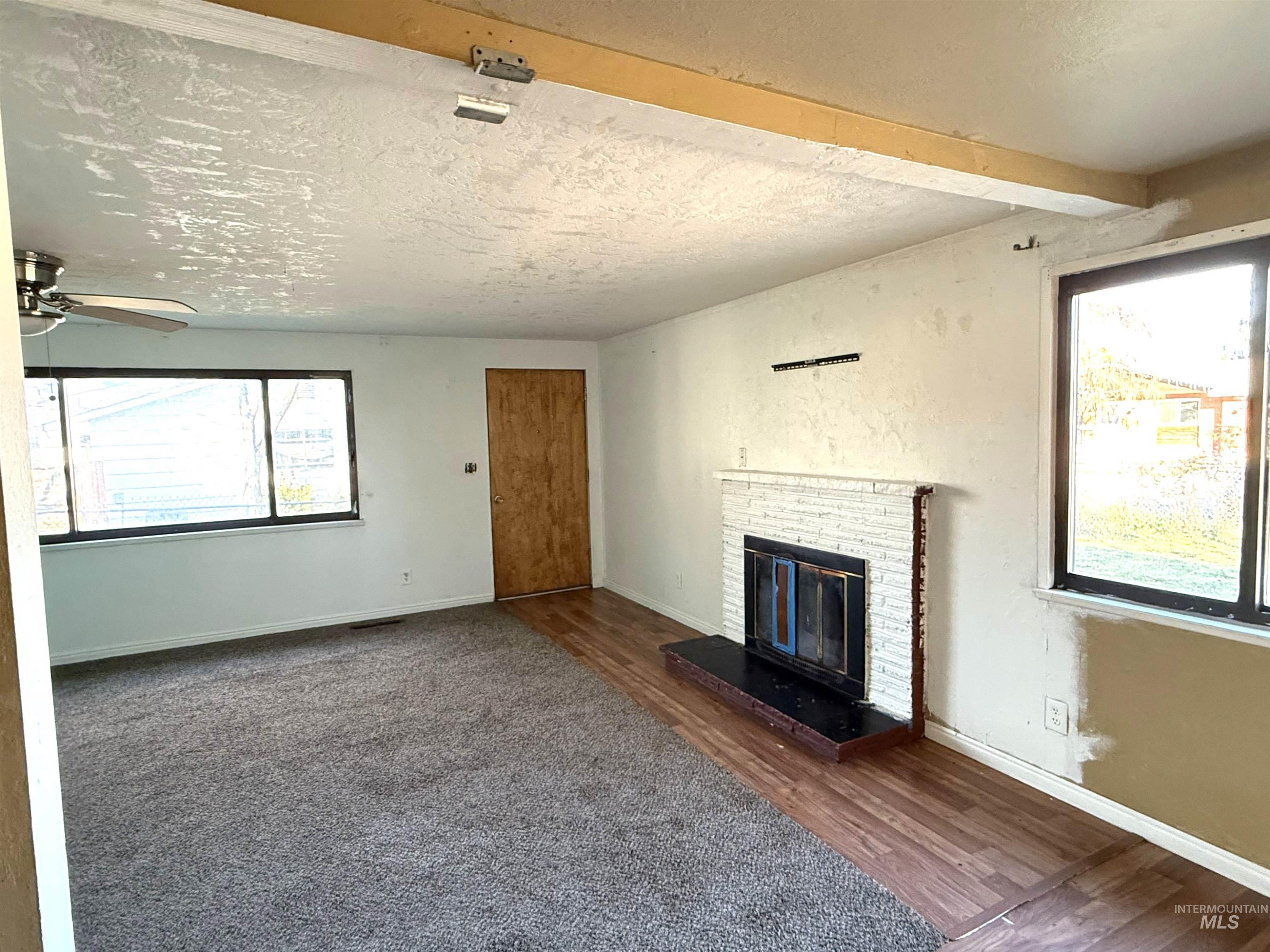 Unfurnished living room with a textured ceiling, beamed ceiling, a fireplace, ceiling fan, and dark wood finished floors
