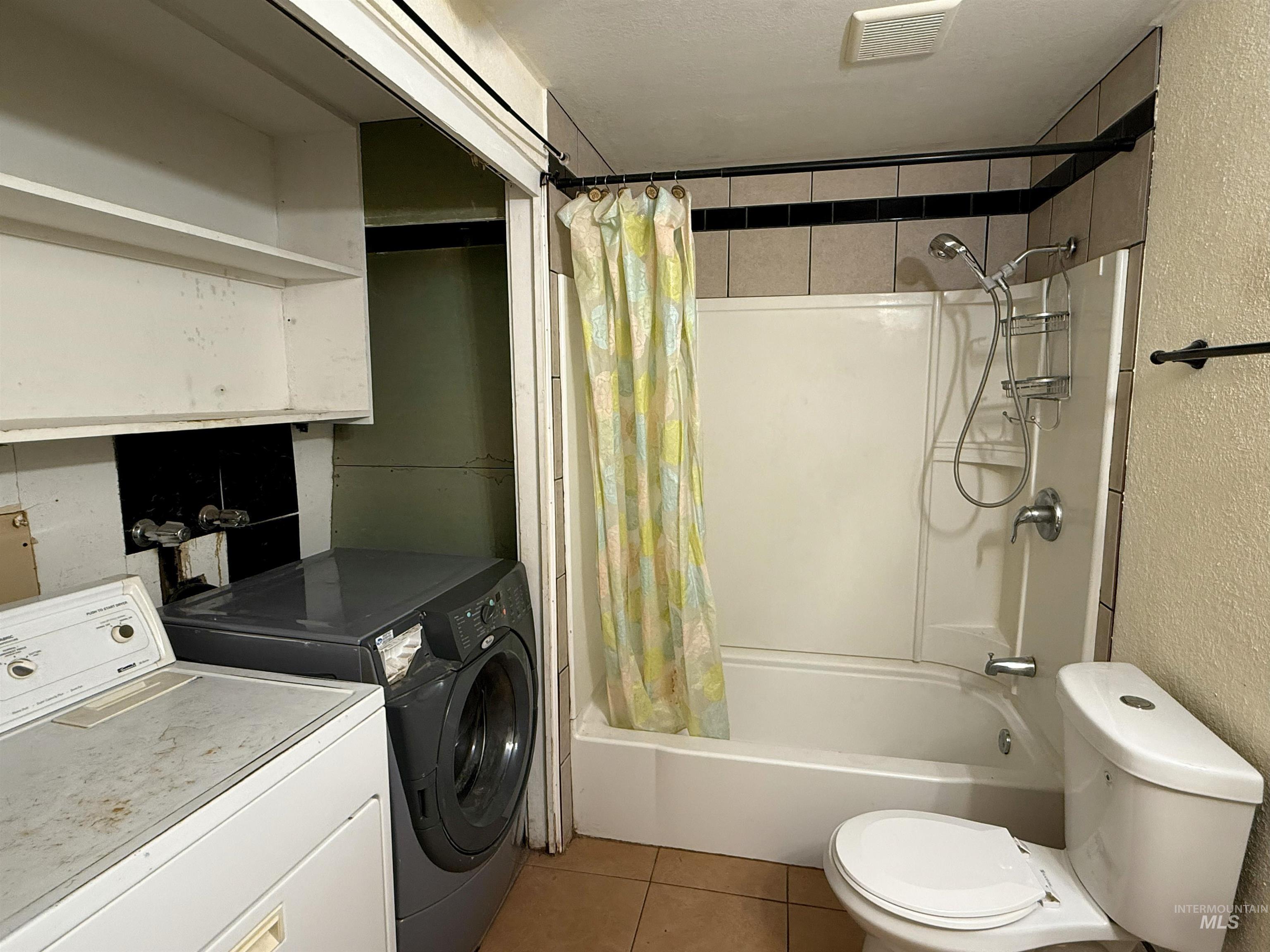 Bathroom with shower / bath combo, a textured wall, tile patterned flooring, and washing machine and dryer