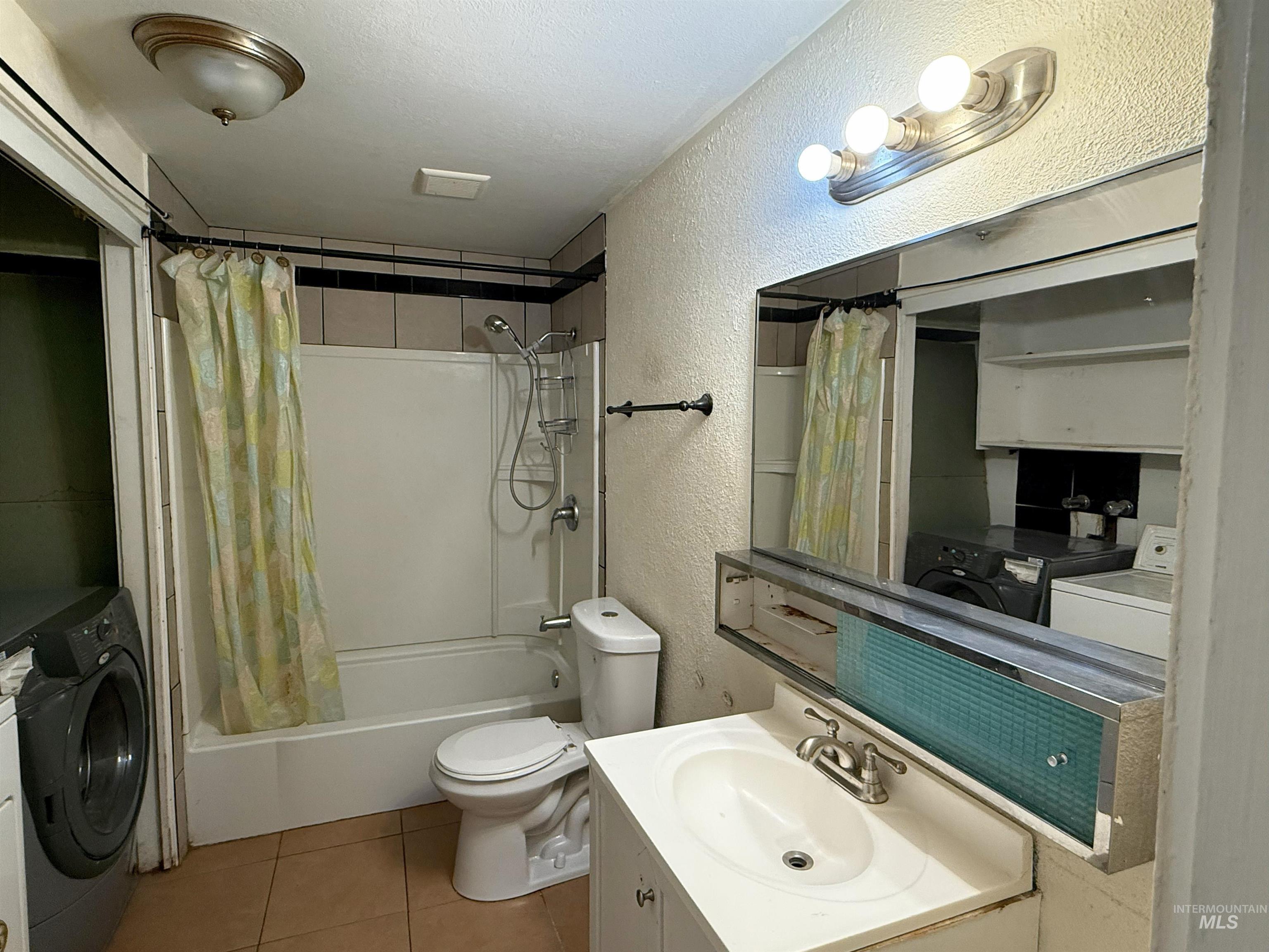 Bathroom with a textured wall, vanity, shower / bath combo, independent washer and dryer, and light tile patterned flooring