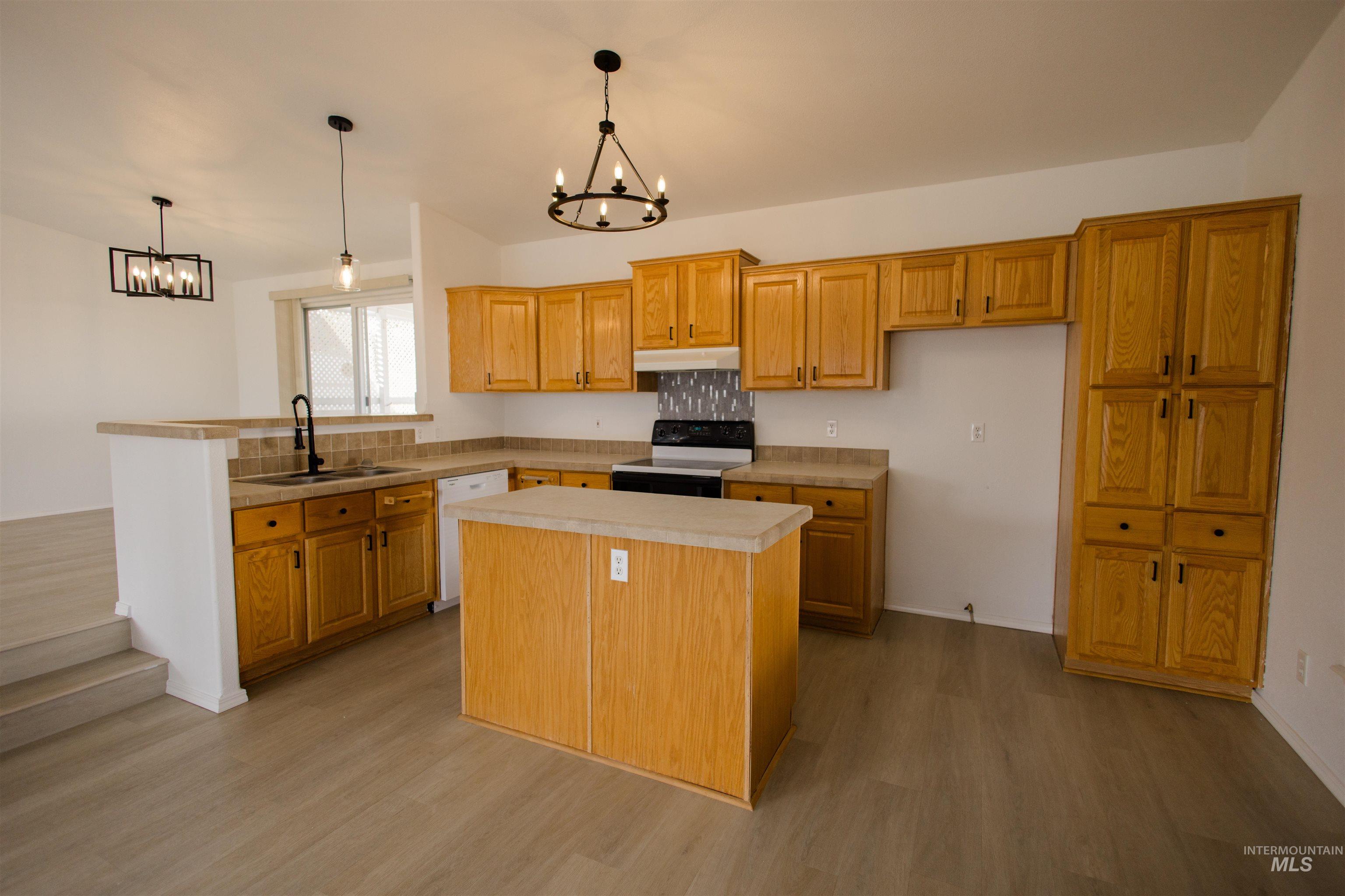 Kitchen with a chandelier, pendant lighting, a peninsula, electric range, and light wood-type flooring