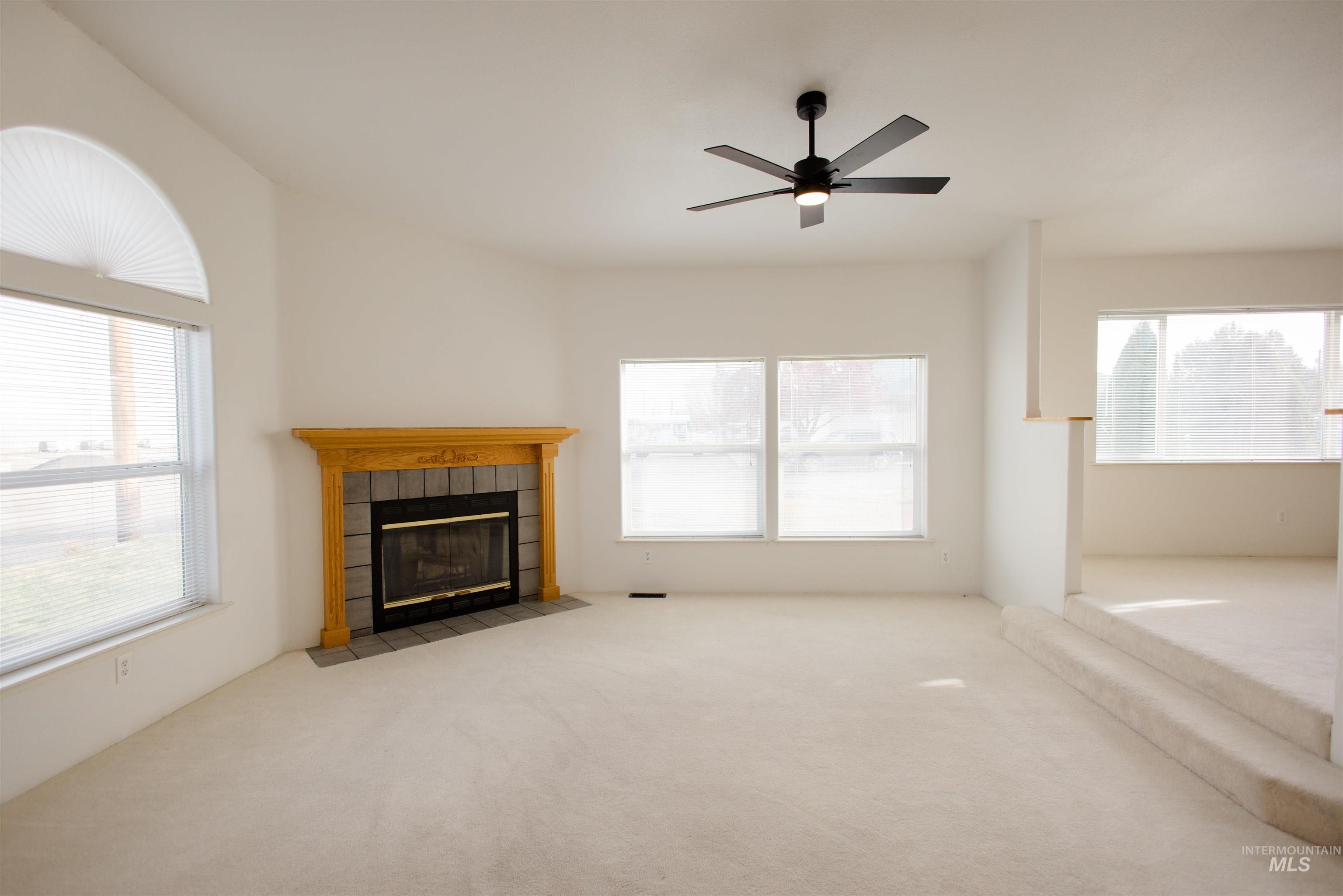 Unfurnished living room with a tiled fireplace, carpet floors, and ceiling fan