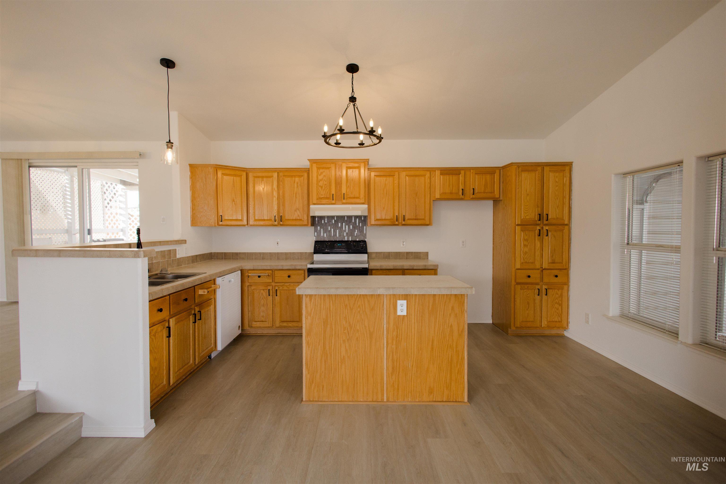 Kitchen featuring light countertops, decorative light fixtures, black electric range, light wood-type flooring, and a chandelier