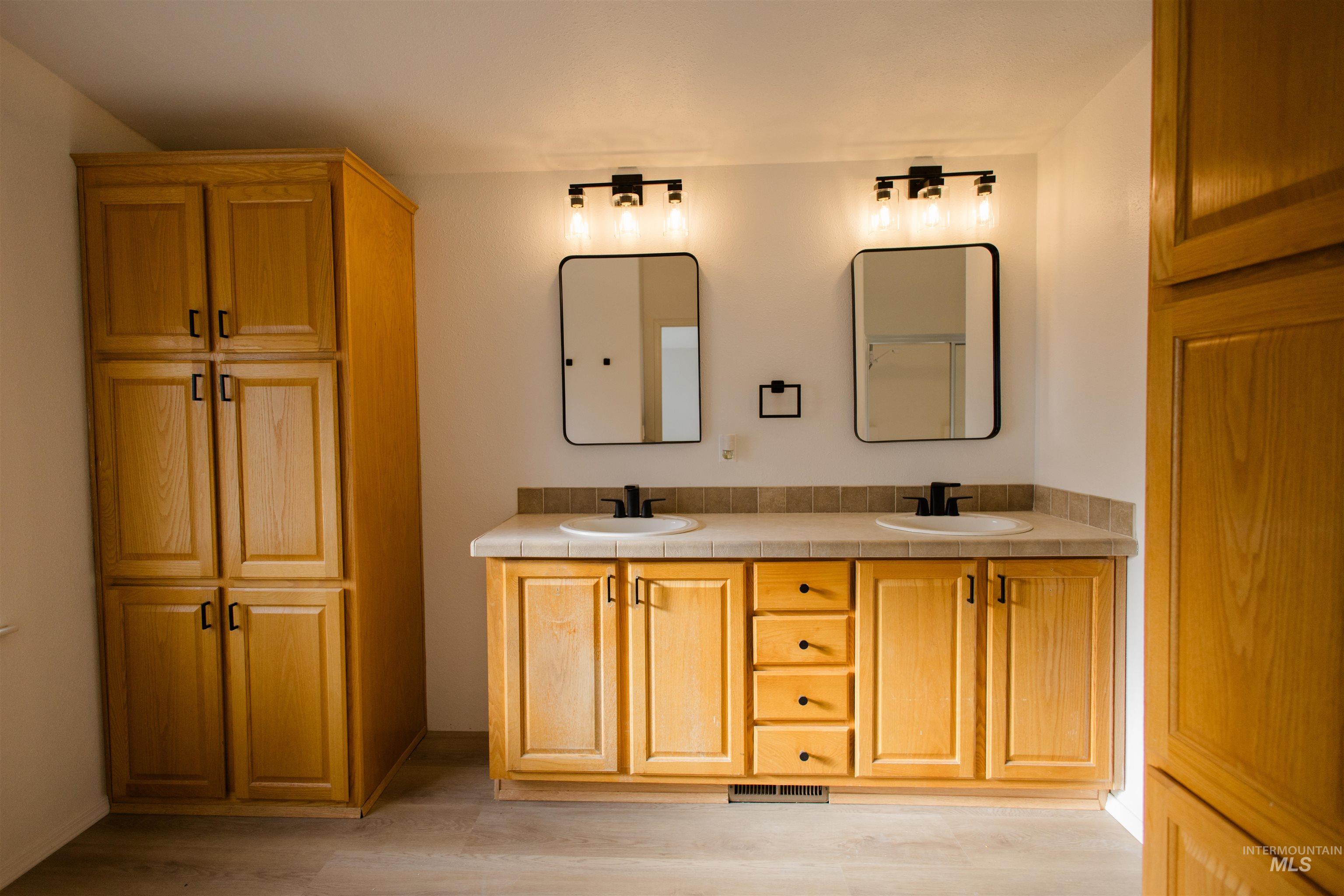 Full bath with double vanity and light wood finished floors