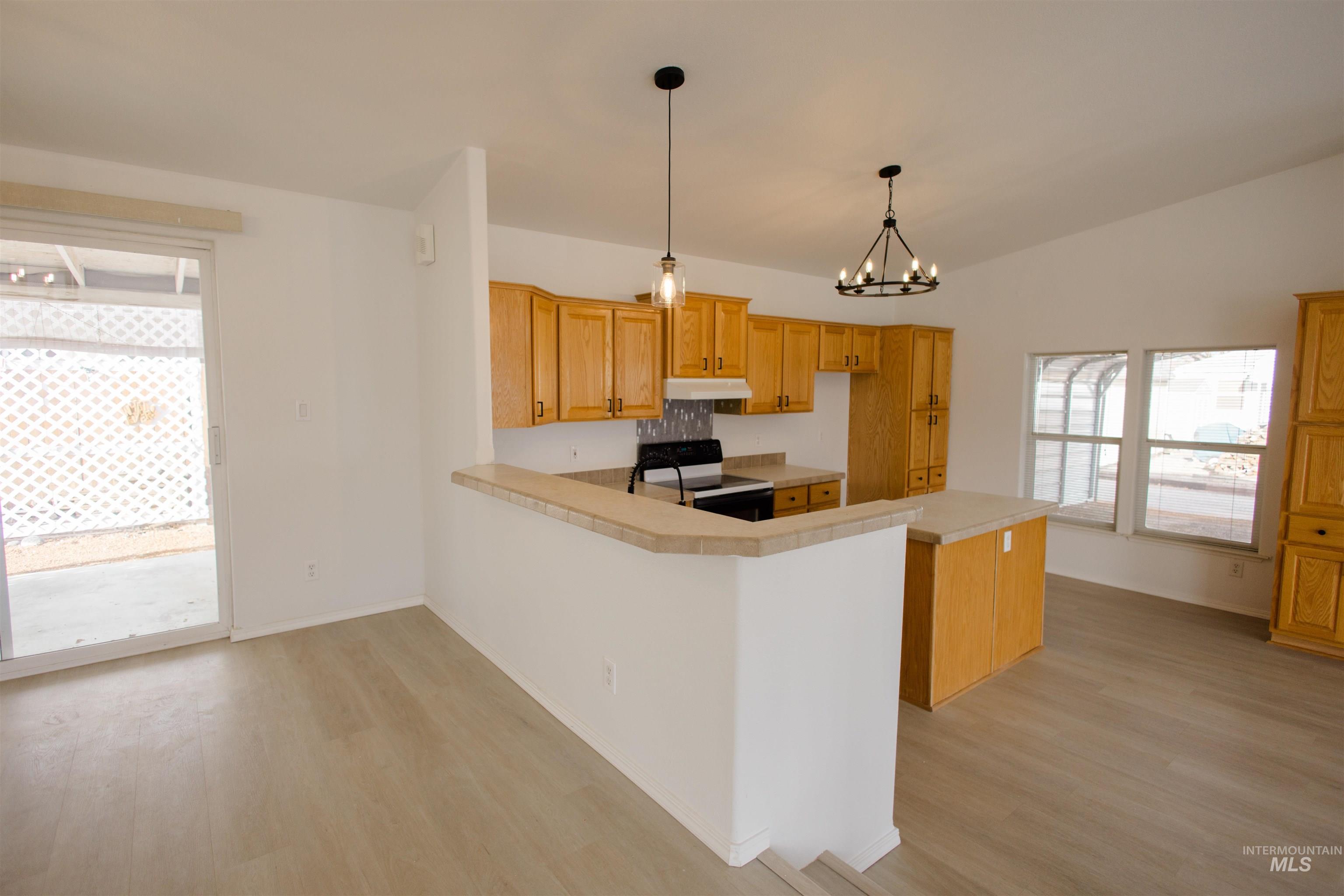 Kitchen with black / electric stove, light countertops, hanging light fixtures, and light wood-style flooring