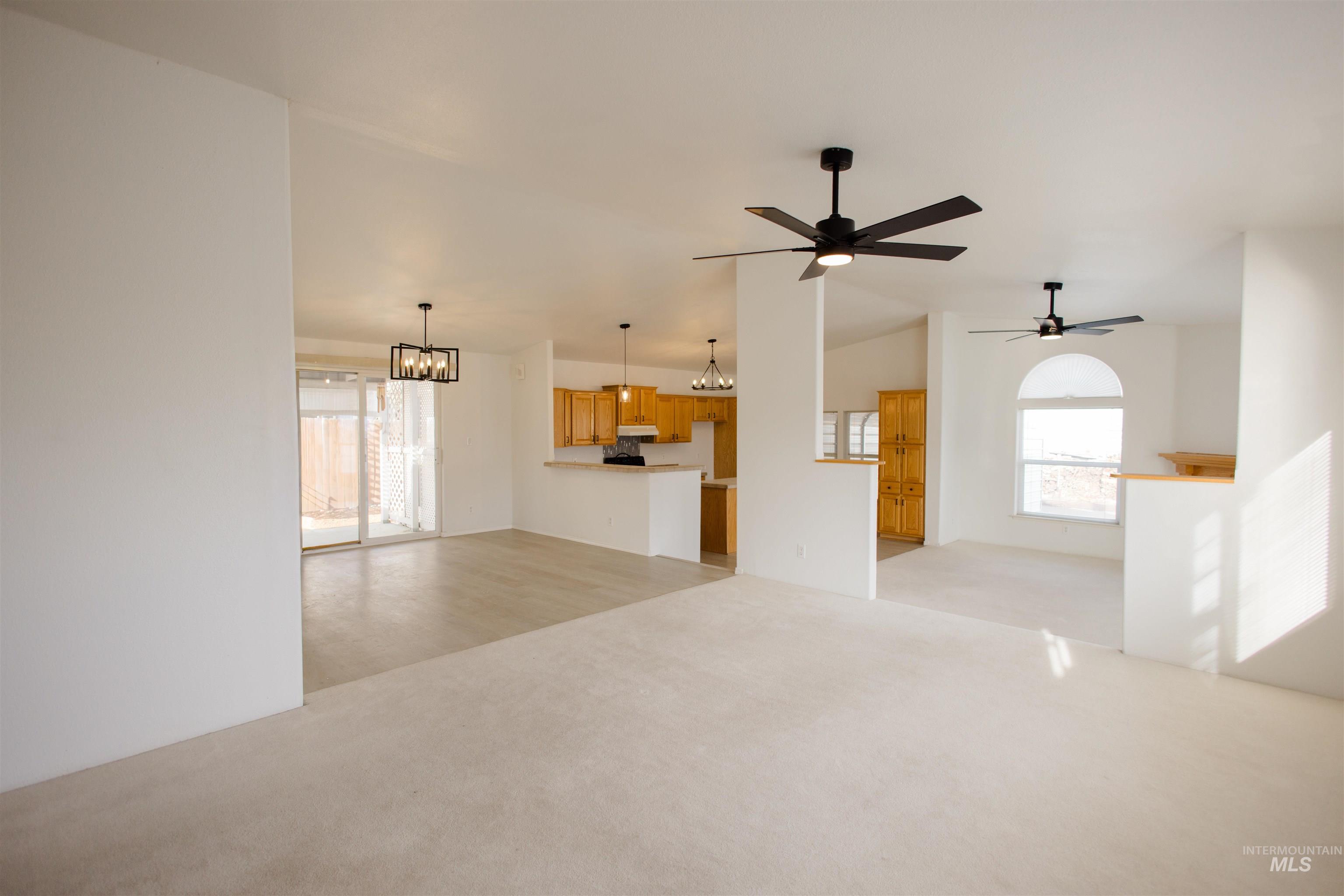 Unfurnished living room featuring a chandelier, light colored carpet, vaulted ceiling, and ceiling fan