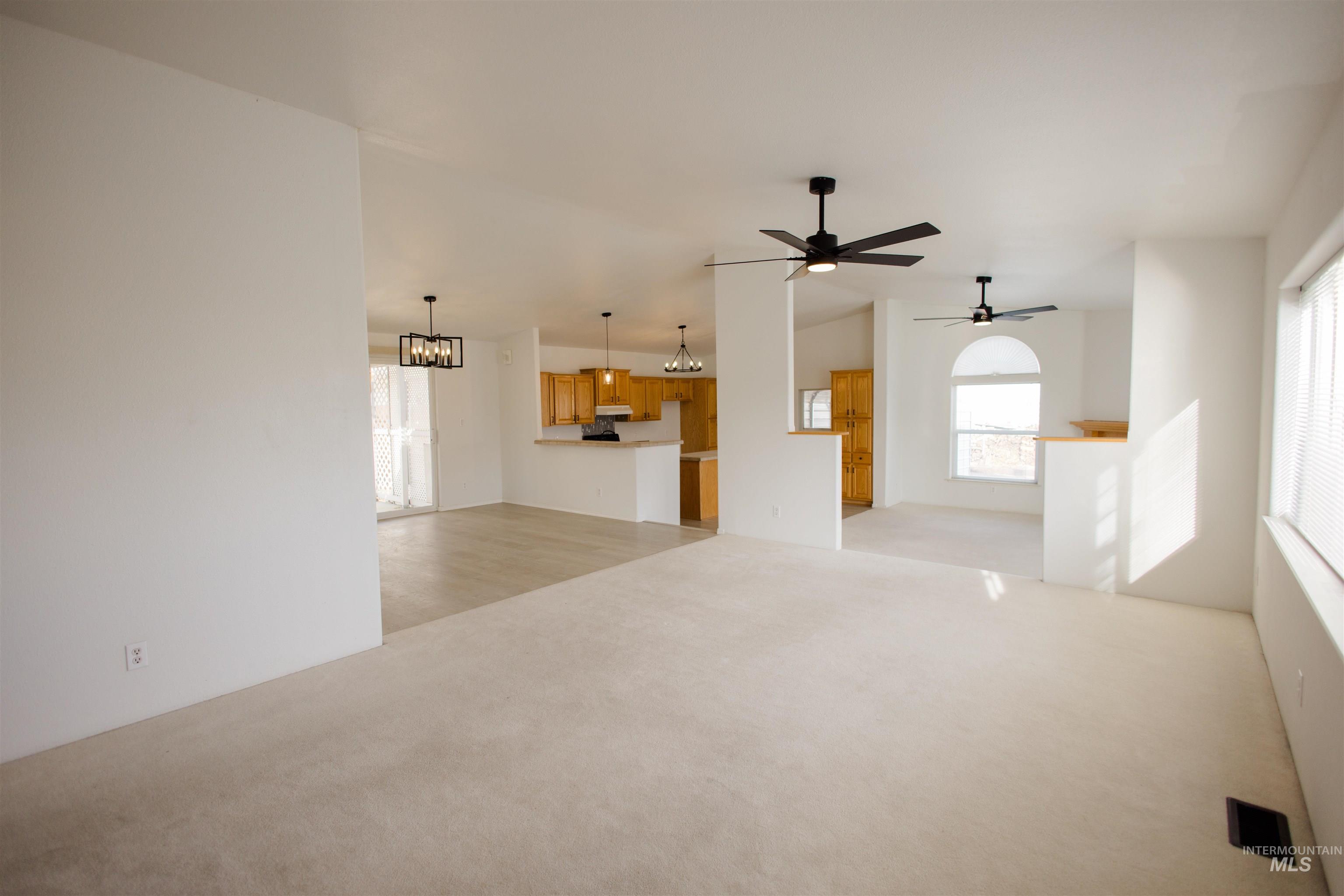 Unfurnished living room featuring a chandelier, light carpet, and a ceiling fan