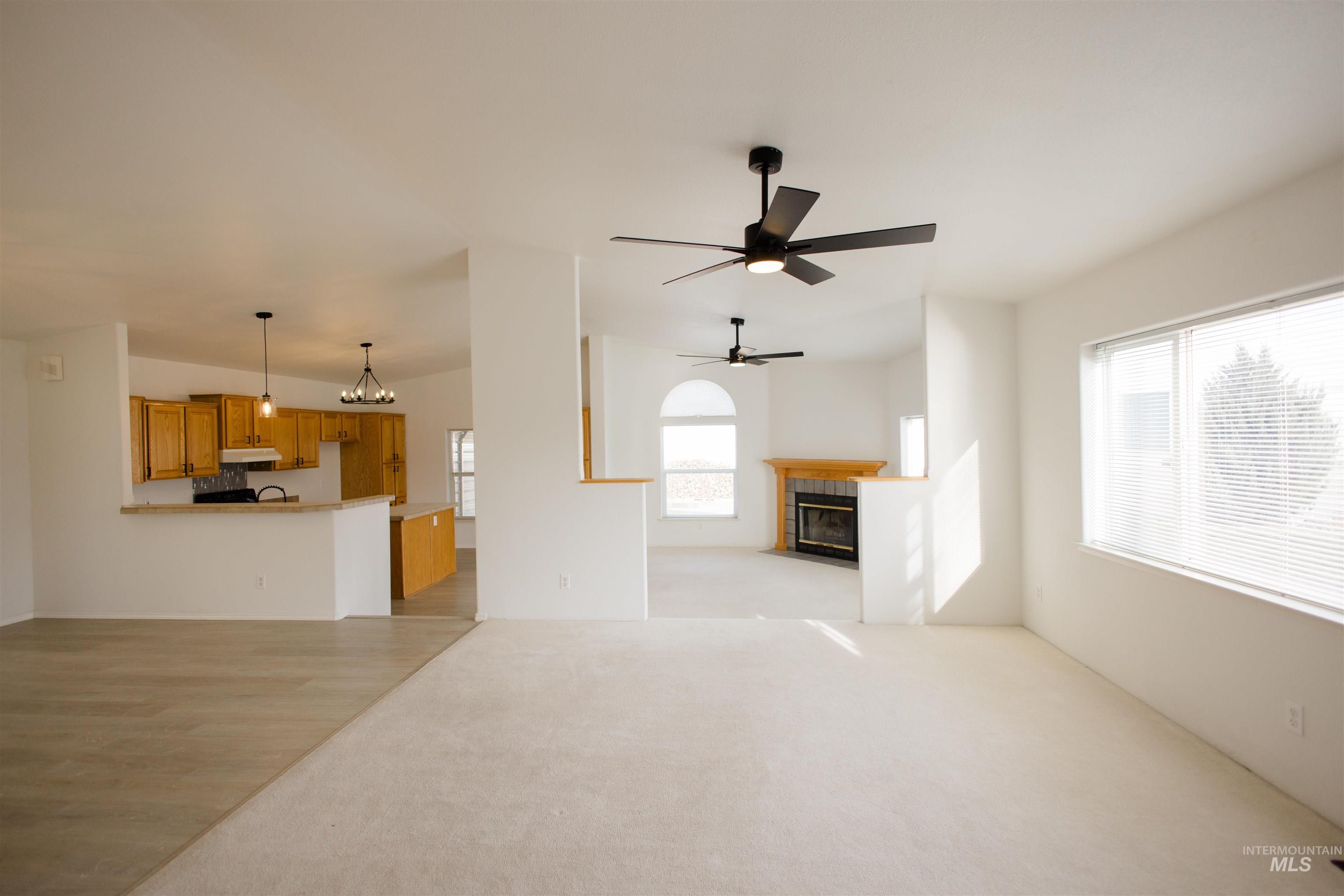 Unfurnished living room featuring a fireplace, a chandelier, ceiling fan, light wood-style floors, and light carpet