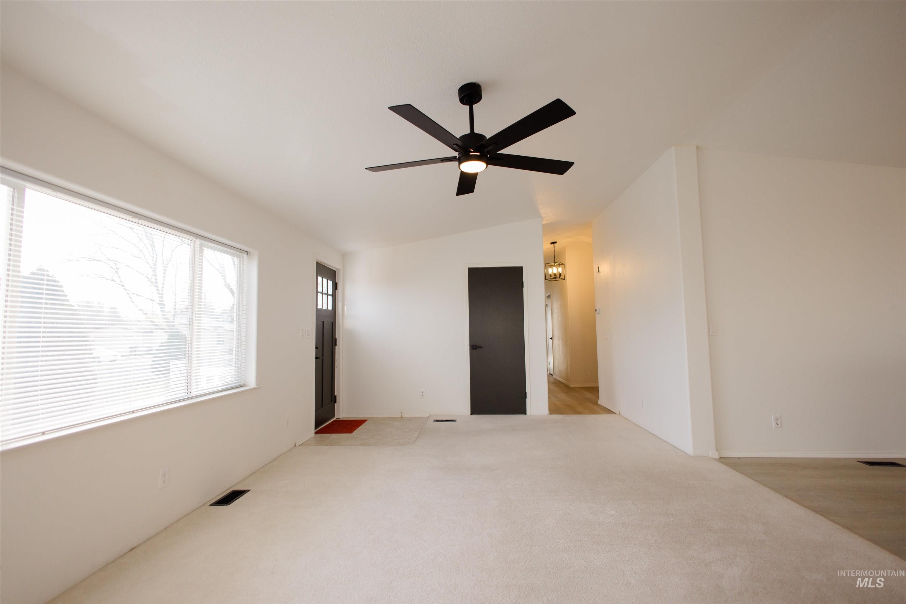 Empty room featuring vaulted ceiling, a ceiling fan, a chandelier, and light carpet