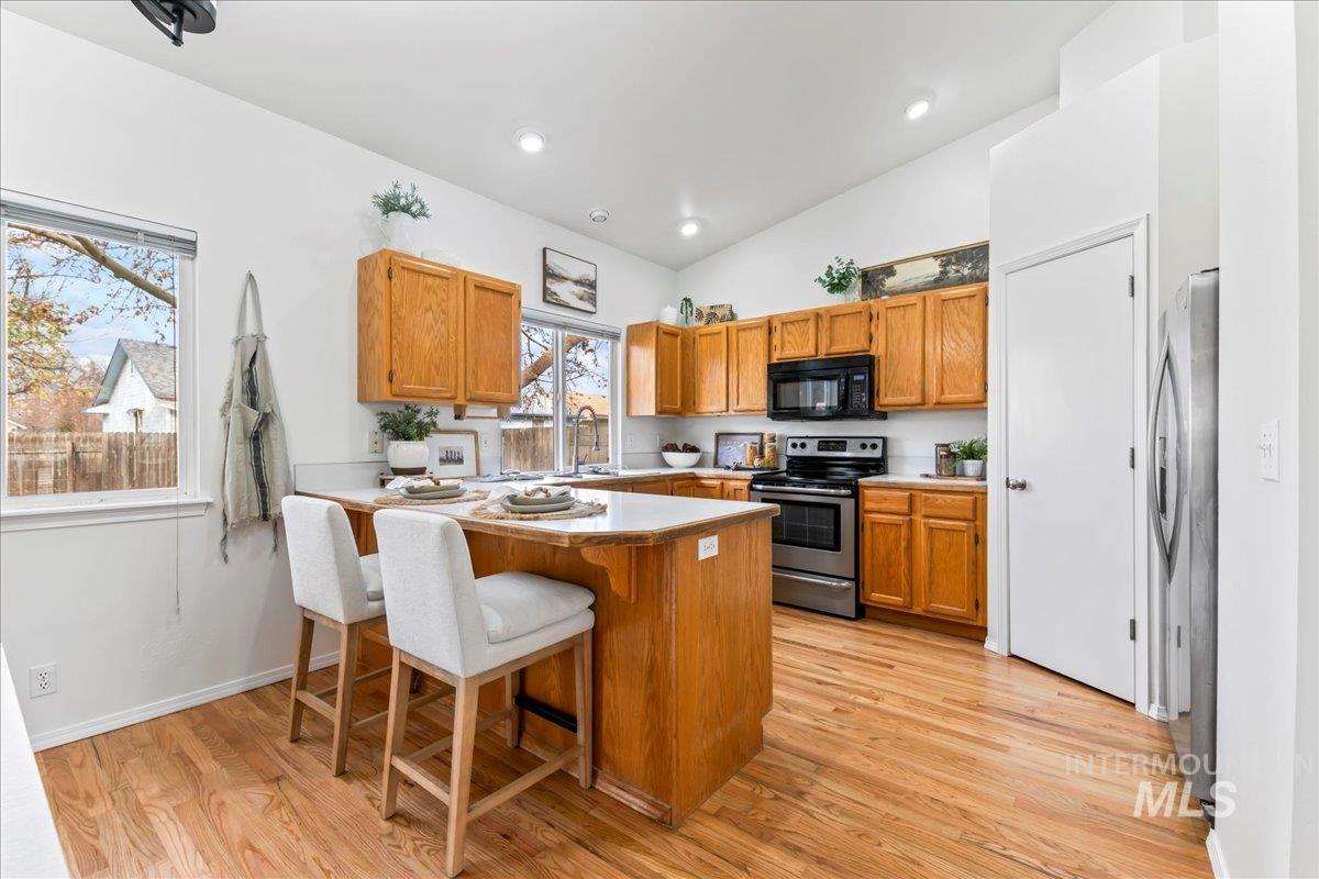 Kitchen featuring brown cabinetry, a peninsula, a kitchen bar, stainless steel appliances, and light wood-style flooring