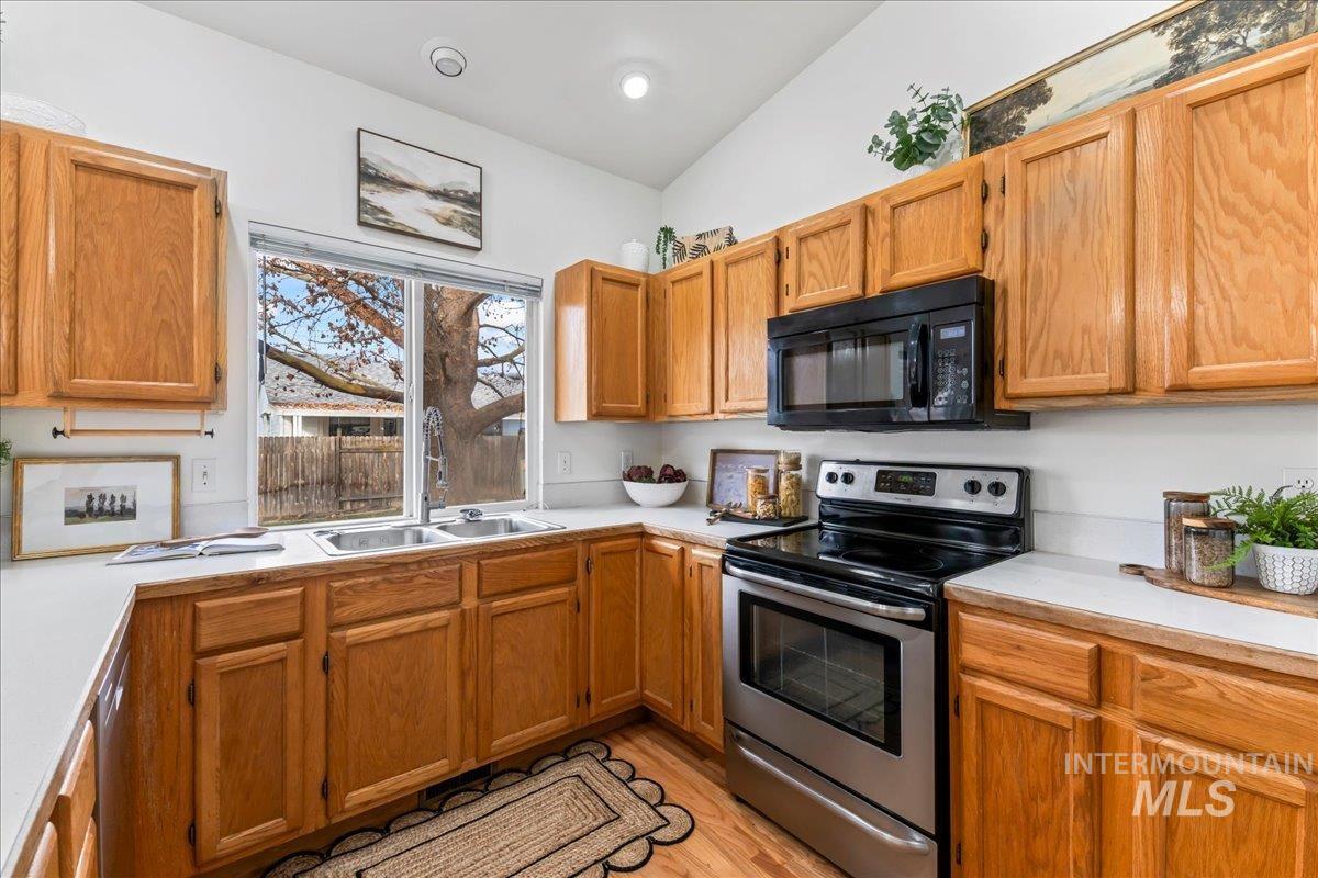 Kitchen with stainless steel electric range, light countertops, black microwave, light wood-type flooring, and vaulted ceiling