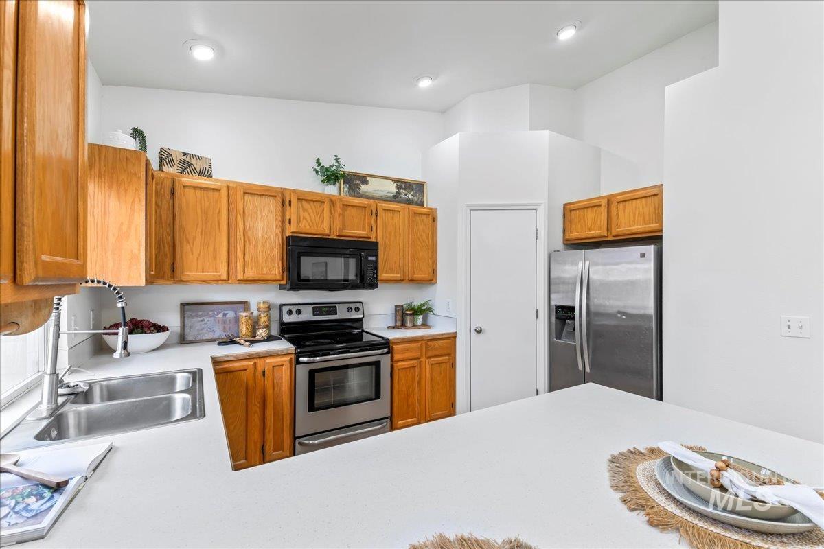Kitchen with appliances with stainless steel finishes, light countertops, brown cabinets, and a high ceiling