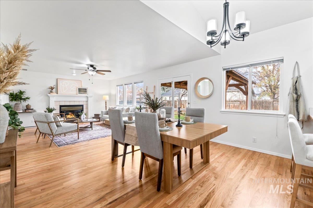 Dining room with a fireplace, light wood-type flooring, a ceiling fan, and a chandelier