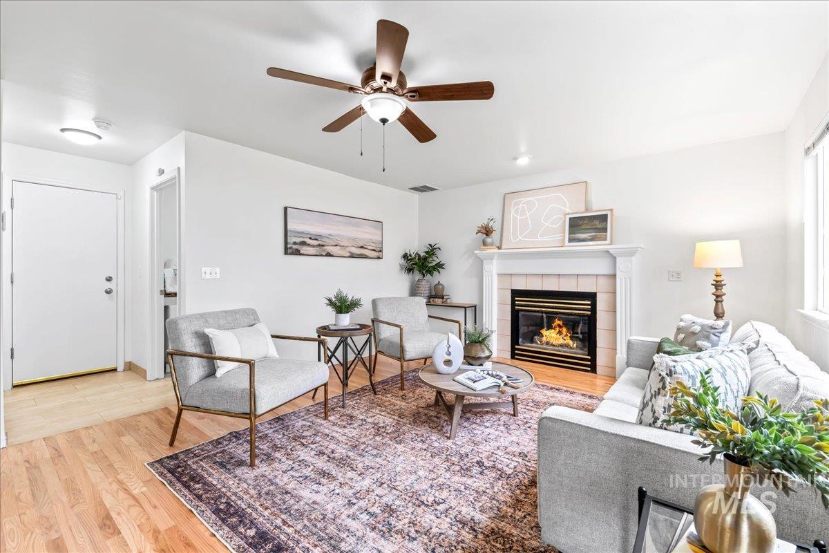 Living room featuring a tile fireplace, light wood finished floors, and ceiling fan