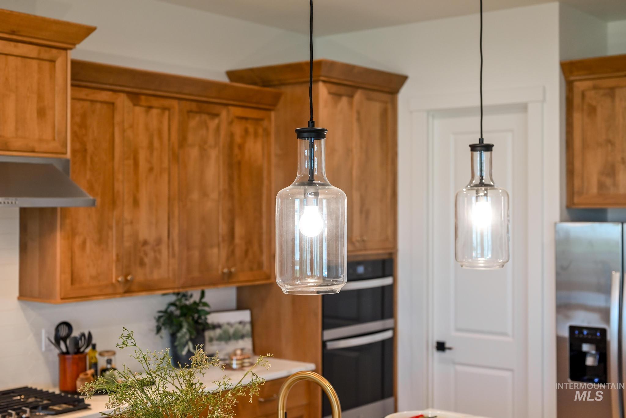 Kitchen with brown cabinetry, stainless steel refrigerator with ice dispenser, decorative light fixtures, under cabinet range hood, and light countertops